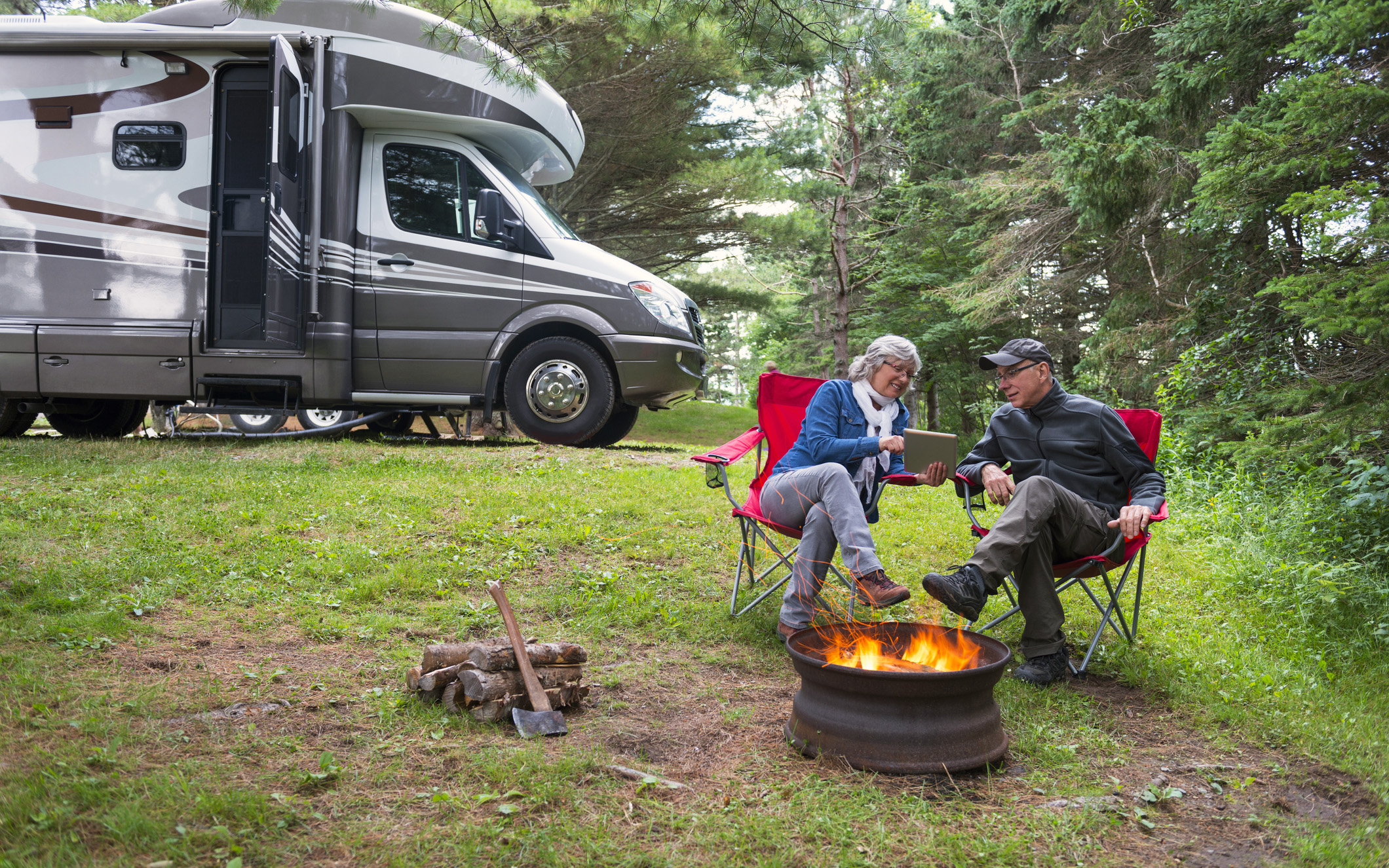 two seniors sitting at campfire with rv in background