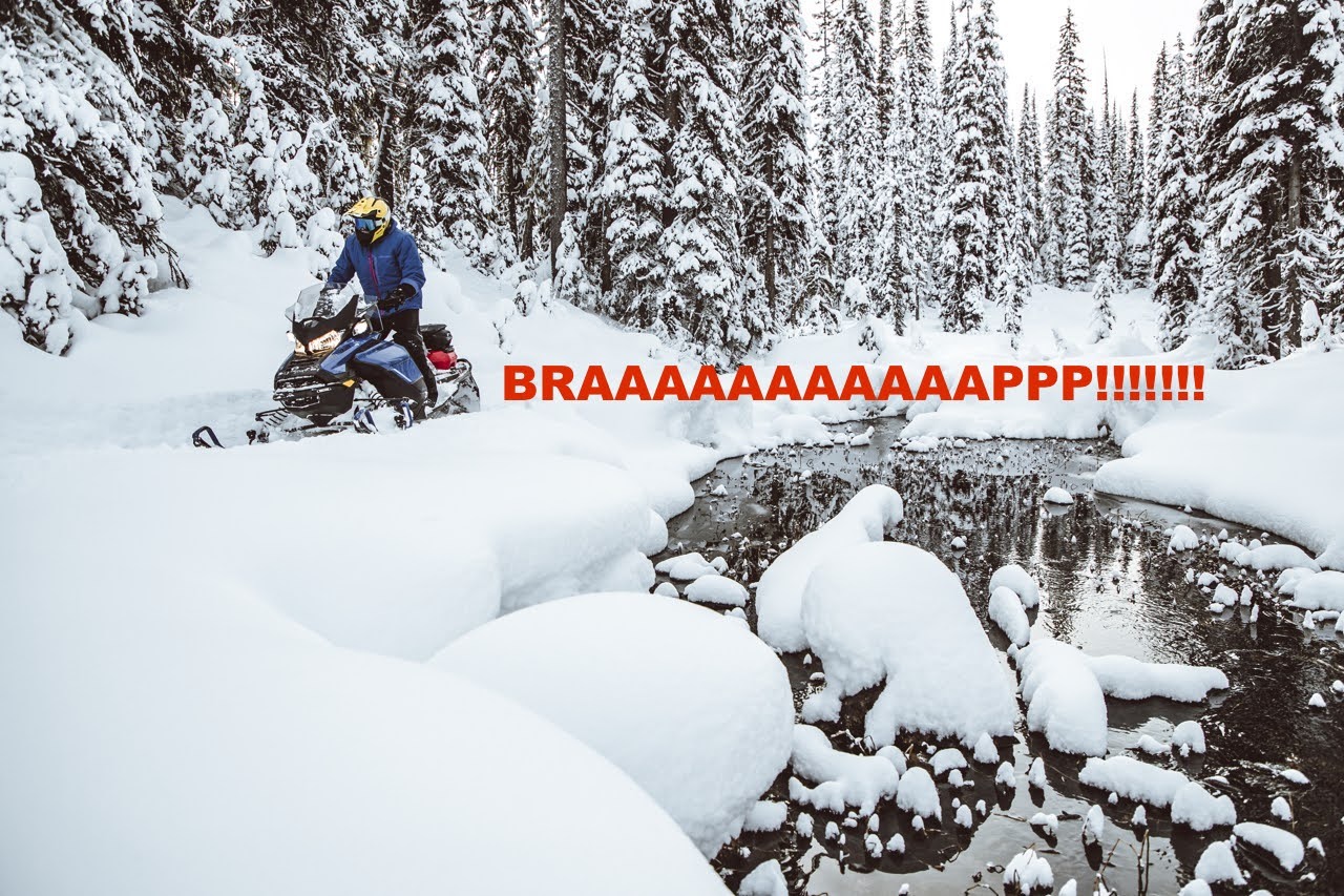 A snowmobiler riding along an open creek, with large fluffy mounds of new snow covering the rocks and forest all around. Typed behind the snowmobile is the word "BRAAAAAAAAAP!!!" in red font.