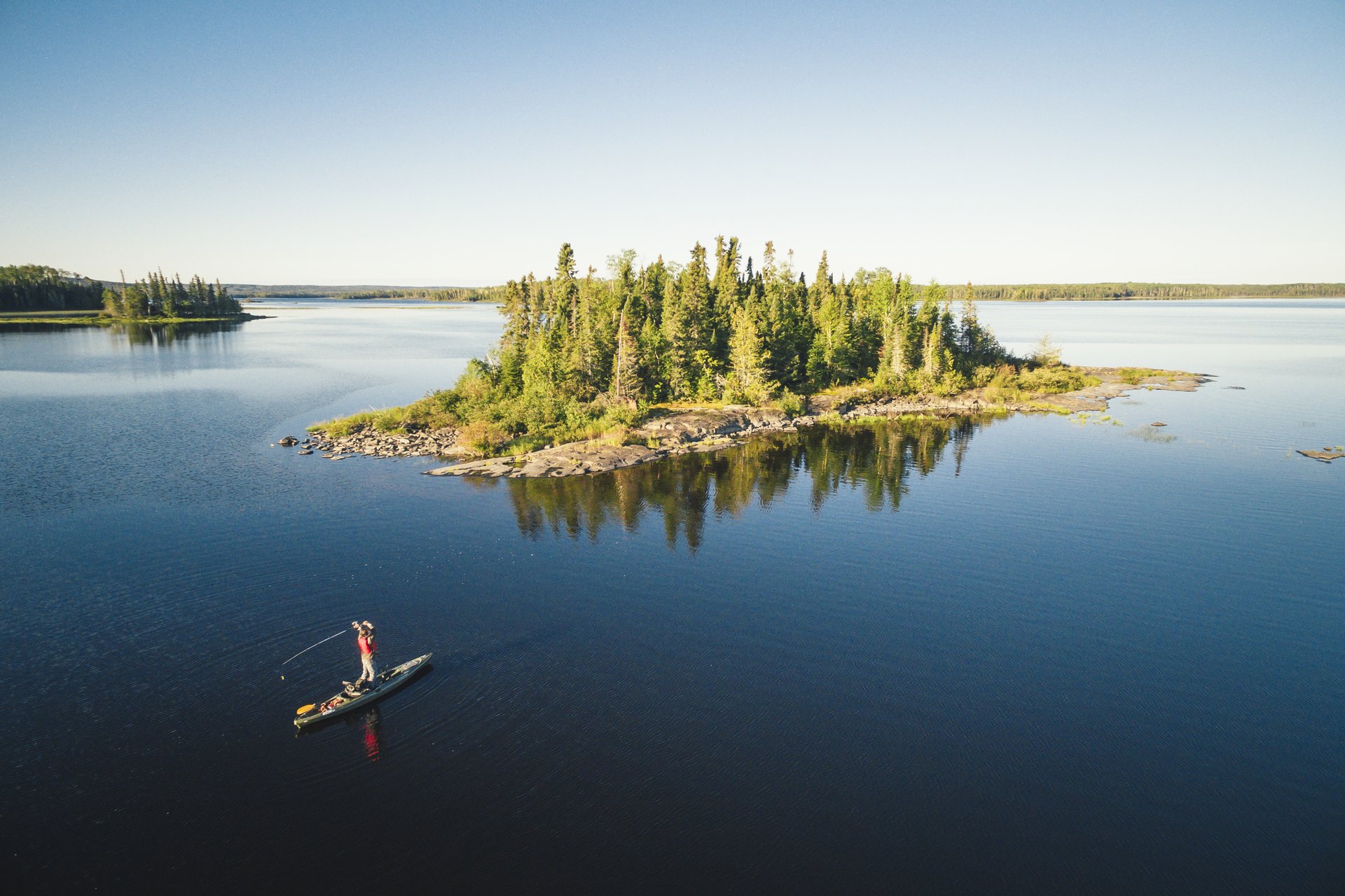 kayak angler stands and casts in front of small island on a Wabakimi lake