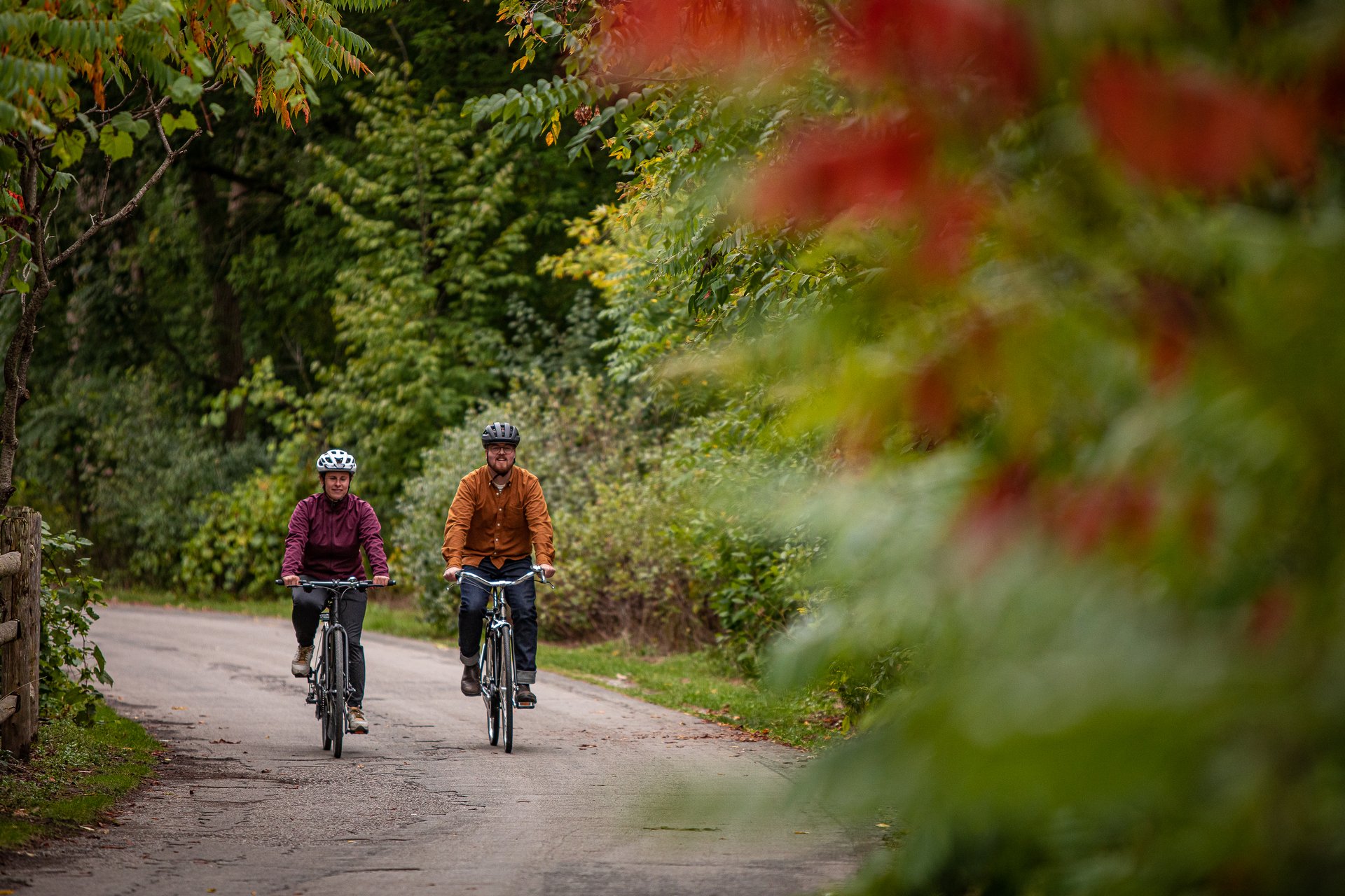 man and woman ride along a rustic roadway with sumac in foreground