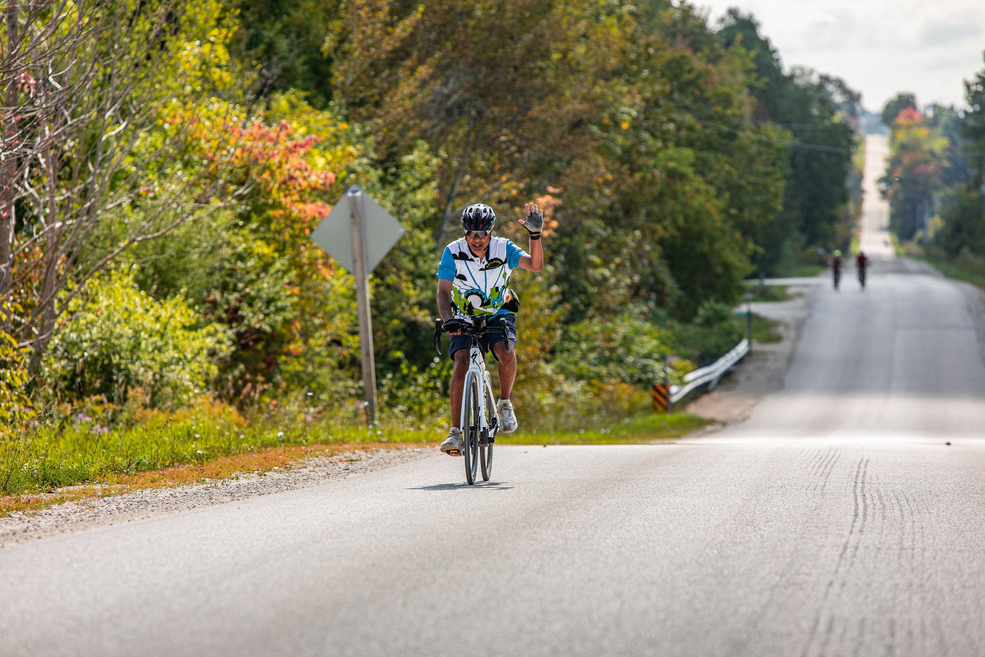 a man waves while cycling along a rural road in Ontario