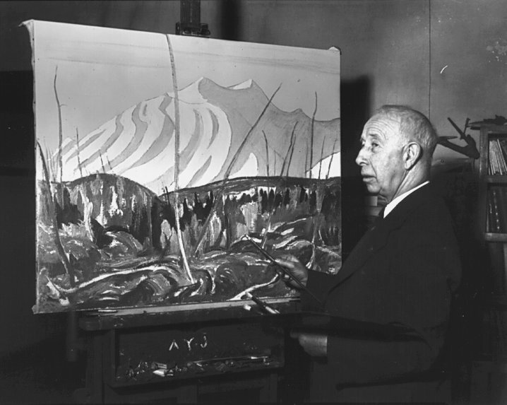 a black and white photograph of artist A.Y. Jackson working at his painting easel.