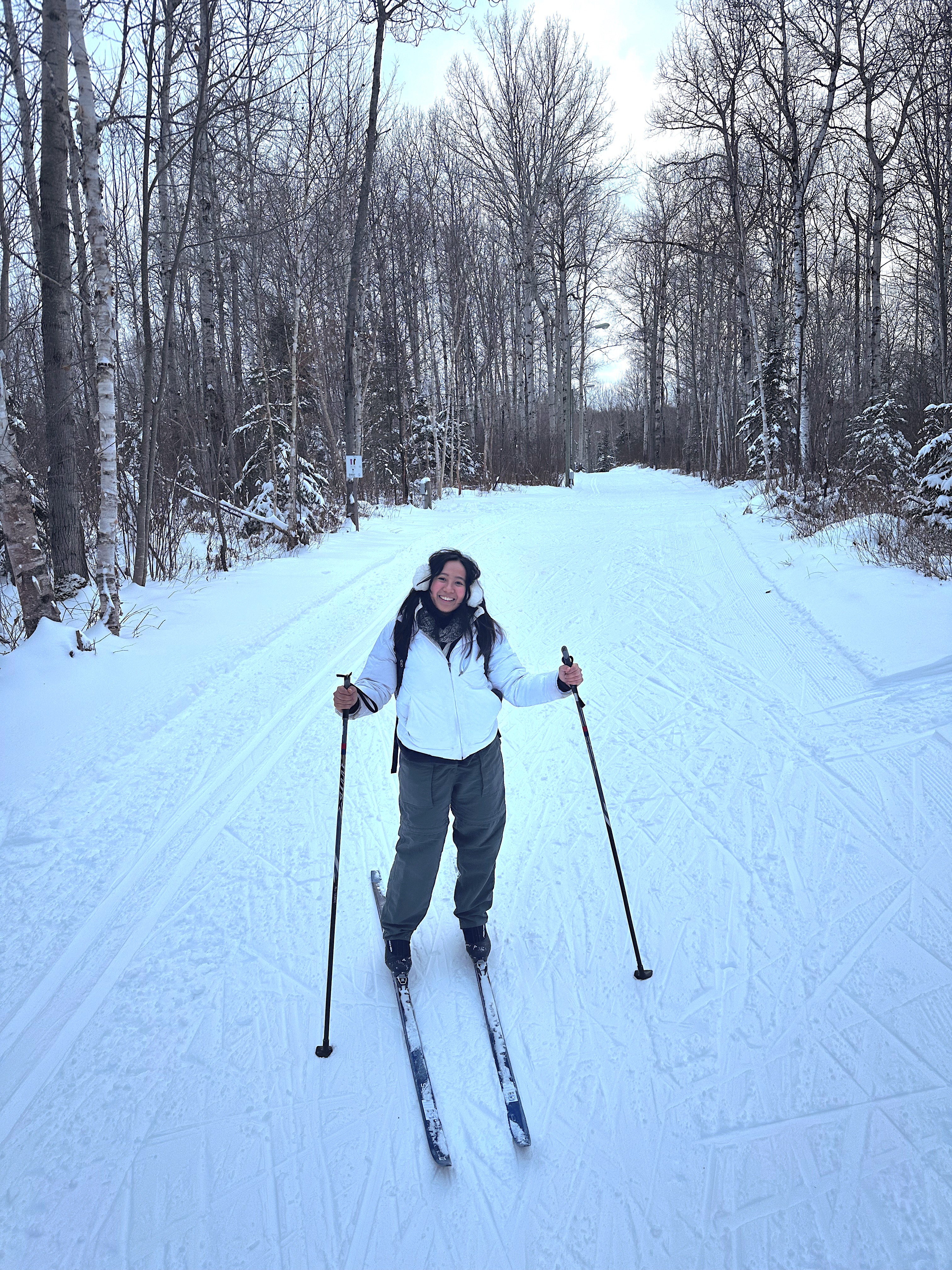 a smiling woman on cross-country skis on a snowy forested ski trail at dusk