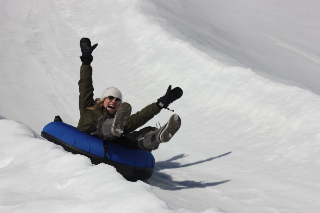 a woman with her arms raised over her head cheers as she slides down a slow slide in an inner tube