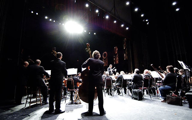 an orchestra performs in front of an audience under bright spotlights