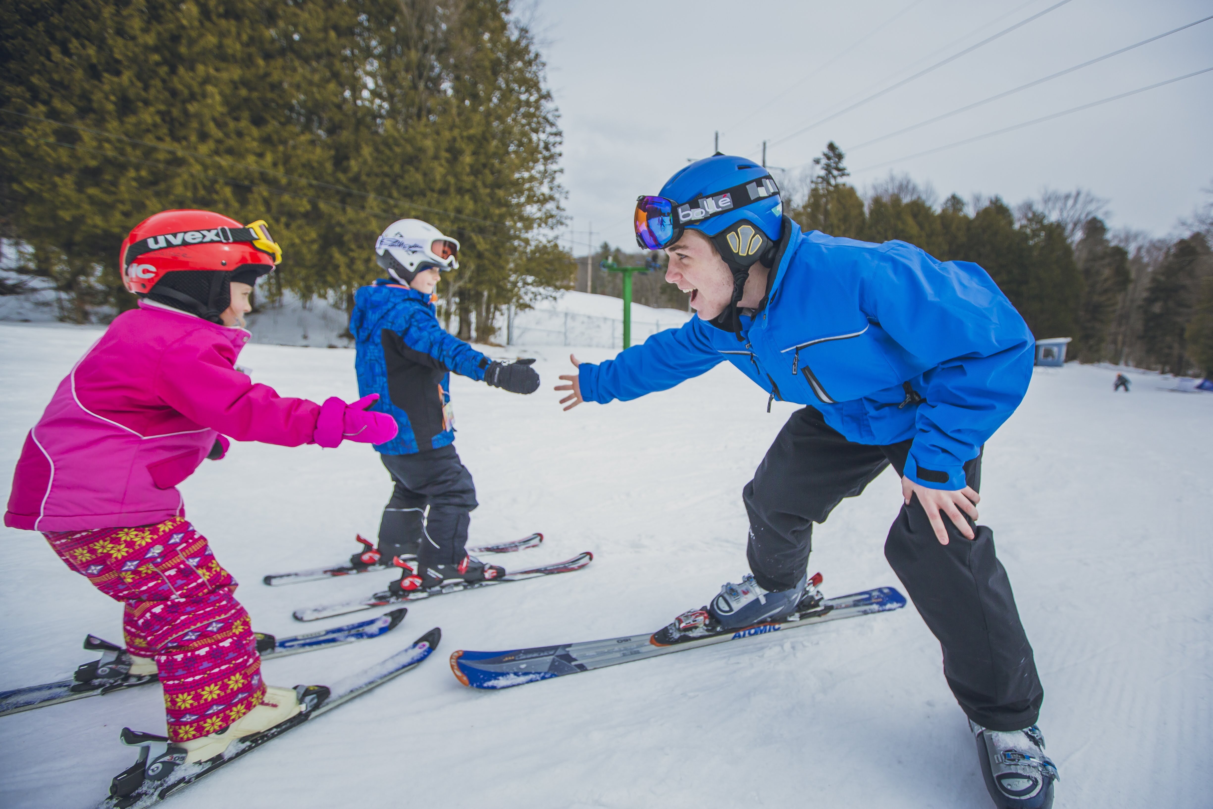 a child in a pink snowsuit and ski gear high-fives their smiling ski coach on a ski hill 