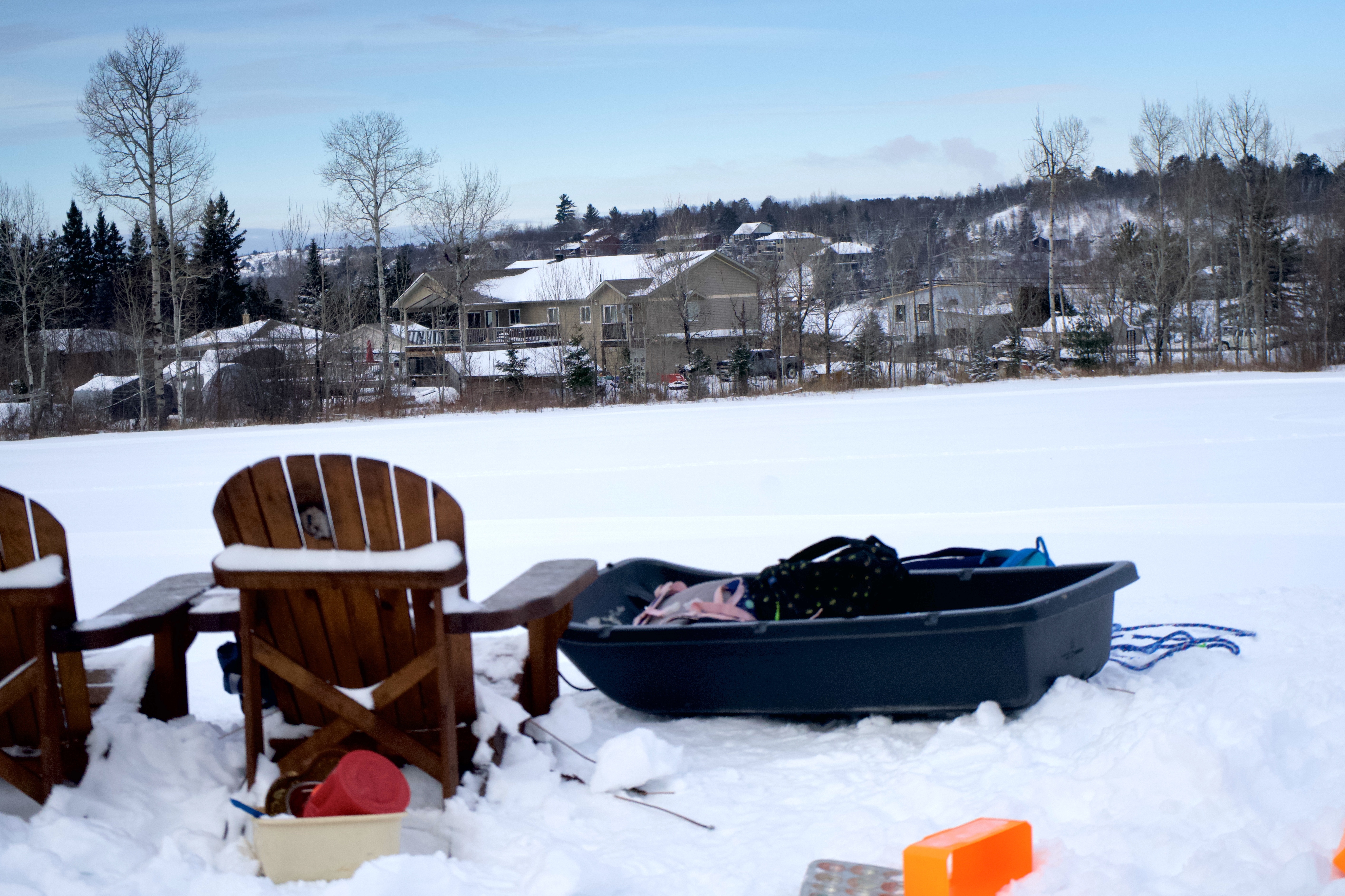 two wooden chairs on the top of a snowy hill overlooking Sudbury, with a sled sitting next to them.