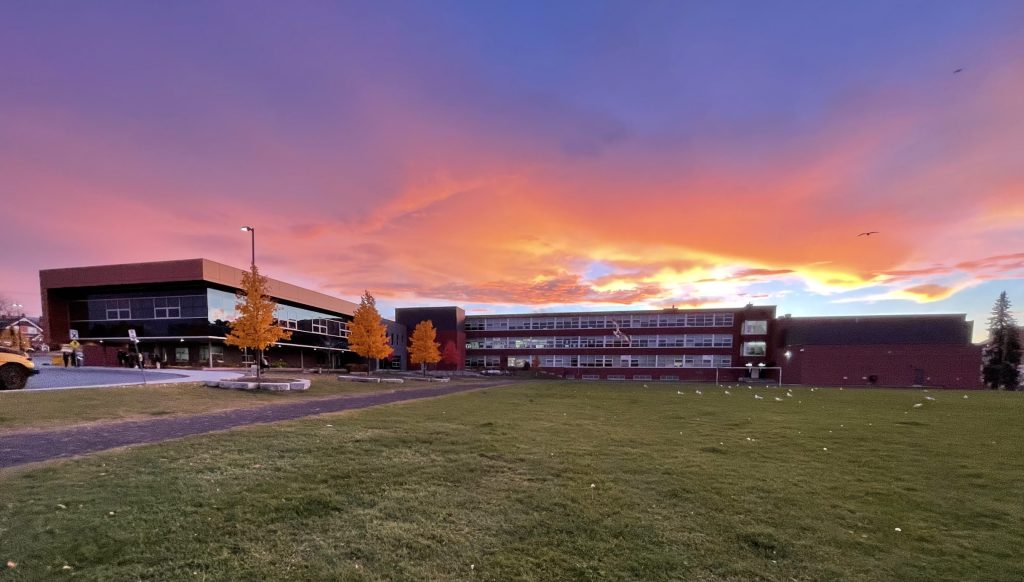 Sudbury Secondary School; a long, single-story brick building with a vivid purple and orange sunset in the background.