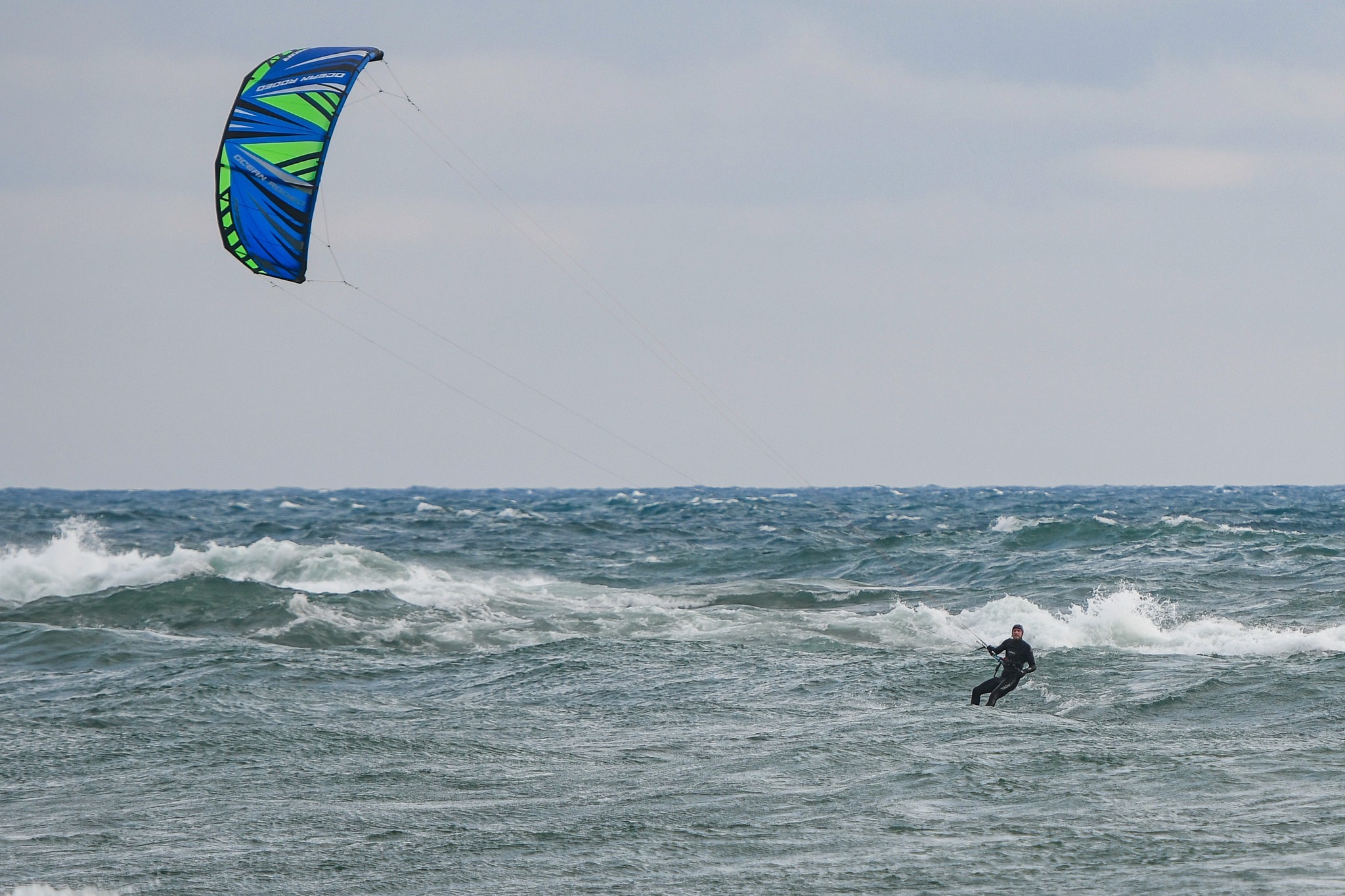 a person kiteboarding on large, grey swells on Lake Superior on a cloudy day.