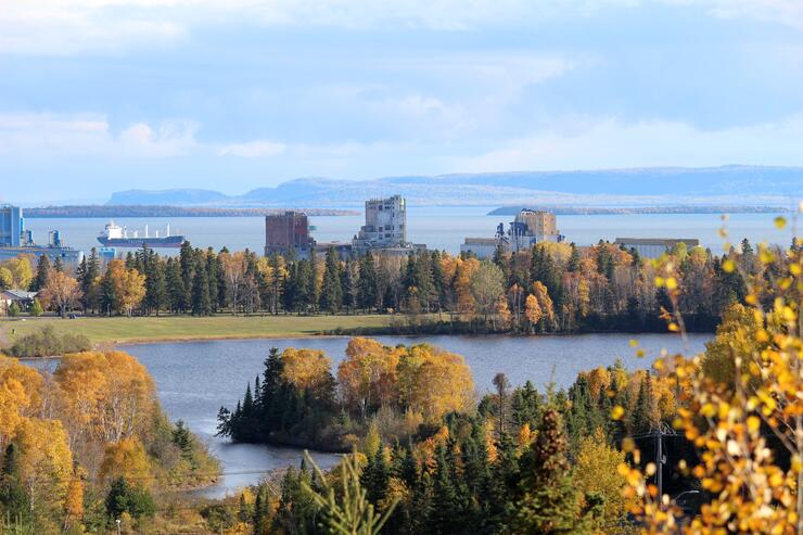 An aerial shot of Boulevard Lake, surrounded by golden autumn trees and green grass with buildings and a Lake Superior Harbour in the distance. 