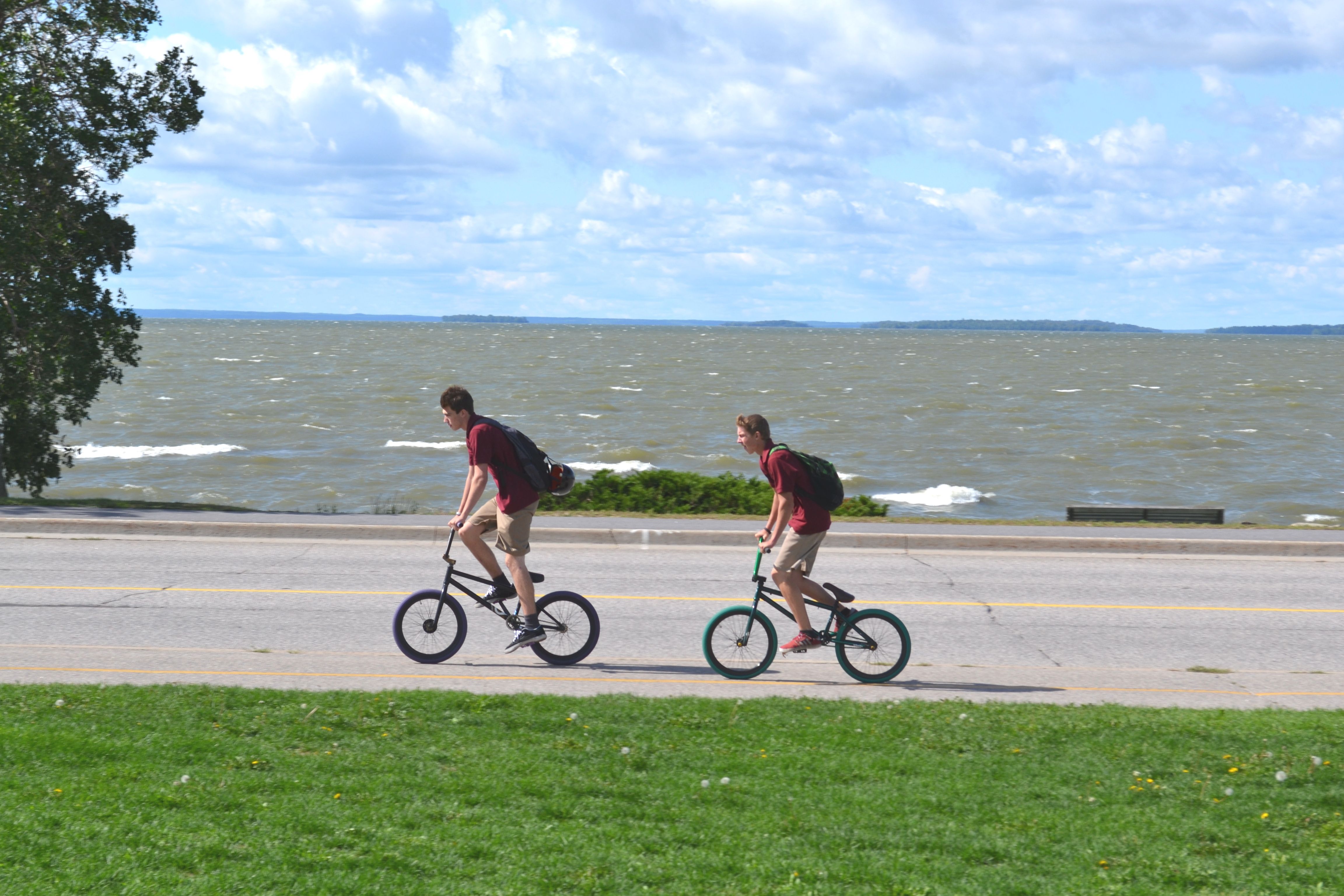 Two boys on bikes ride down a paved bike trail along Lake Nipissing on a summer day.