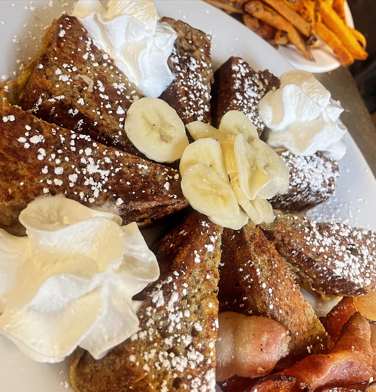 a delicious-looking plate of french toast with whipped cream, powdered sugar and bananas.