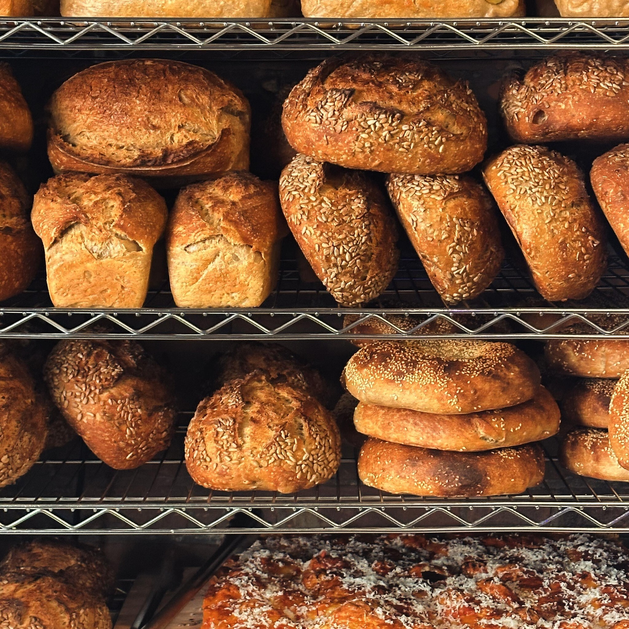 a metal bakery shelf filled completely with differently-shaped loaves of artisanal bread.