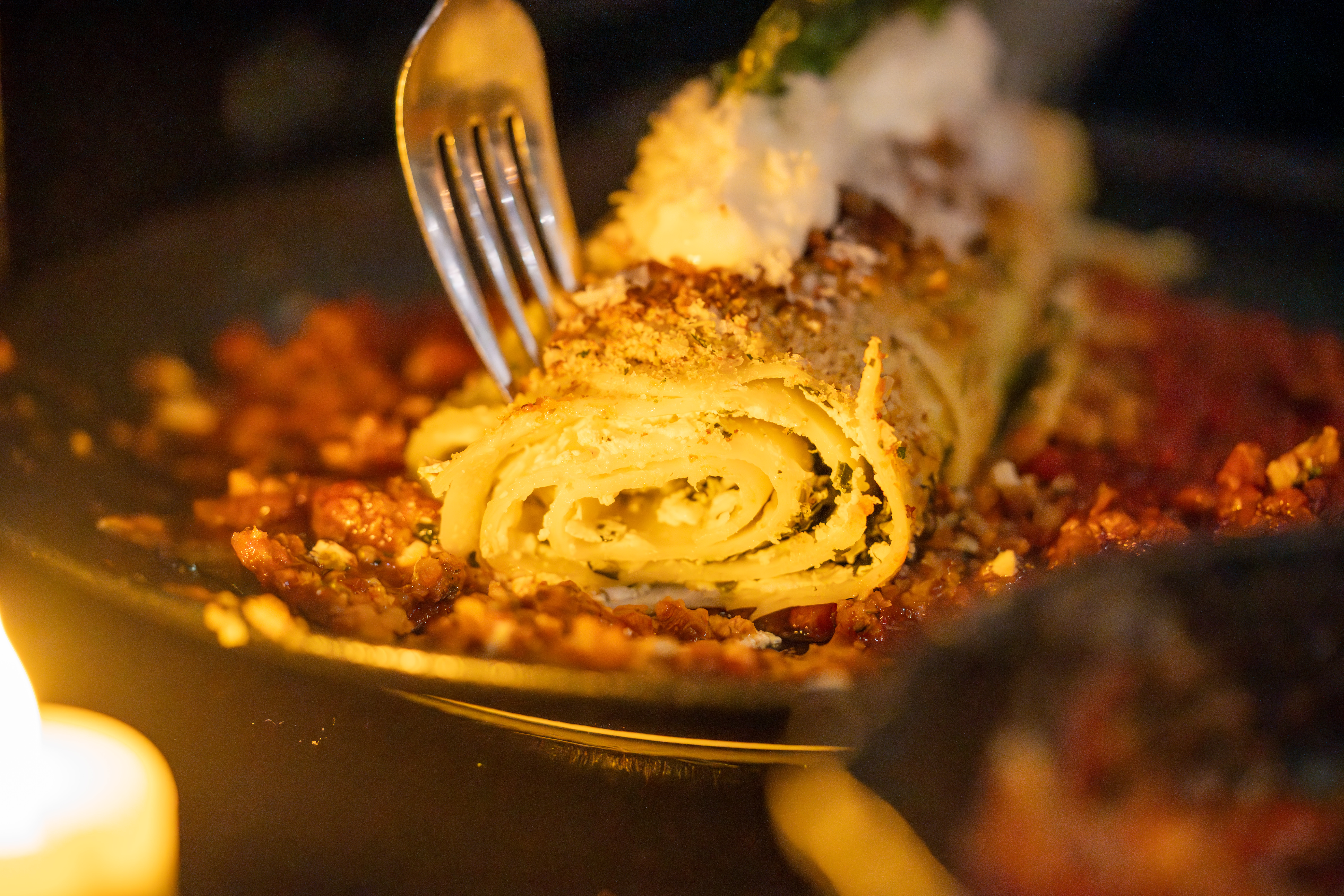 a delicious-looking pasta dish with fresh tomato sauce and grated cheeses with a fork placed in it, lit by candle light. 