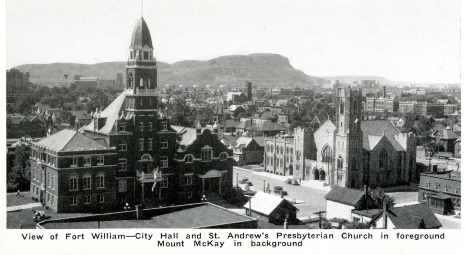 An antique black and white photograph of old Fort William with a large church in the foreground and Mount Mckay on the horizon.