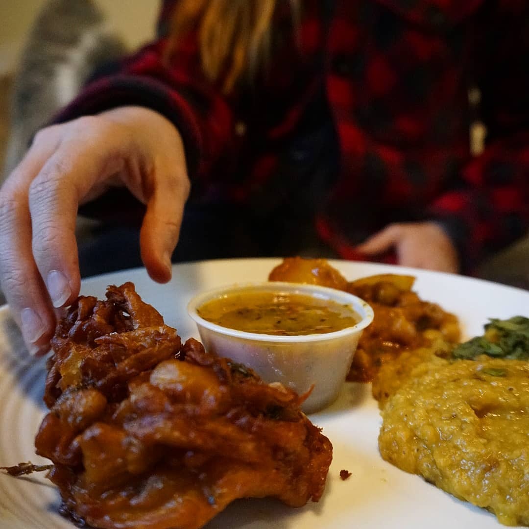 A hand reaches for a plate of Indra's tarka daal, chana masala and pakoras