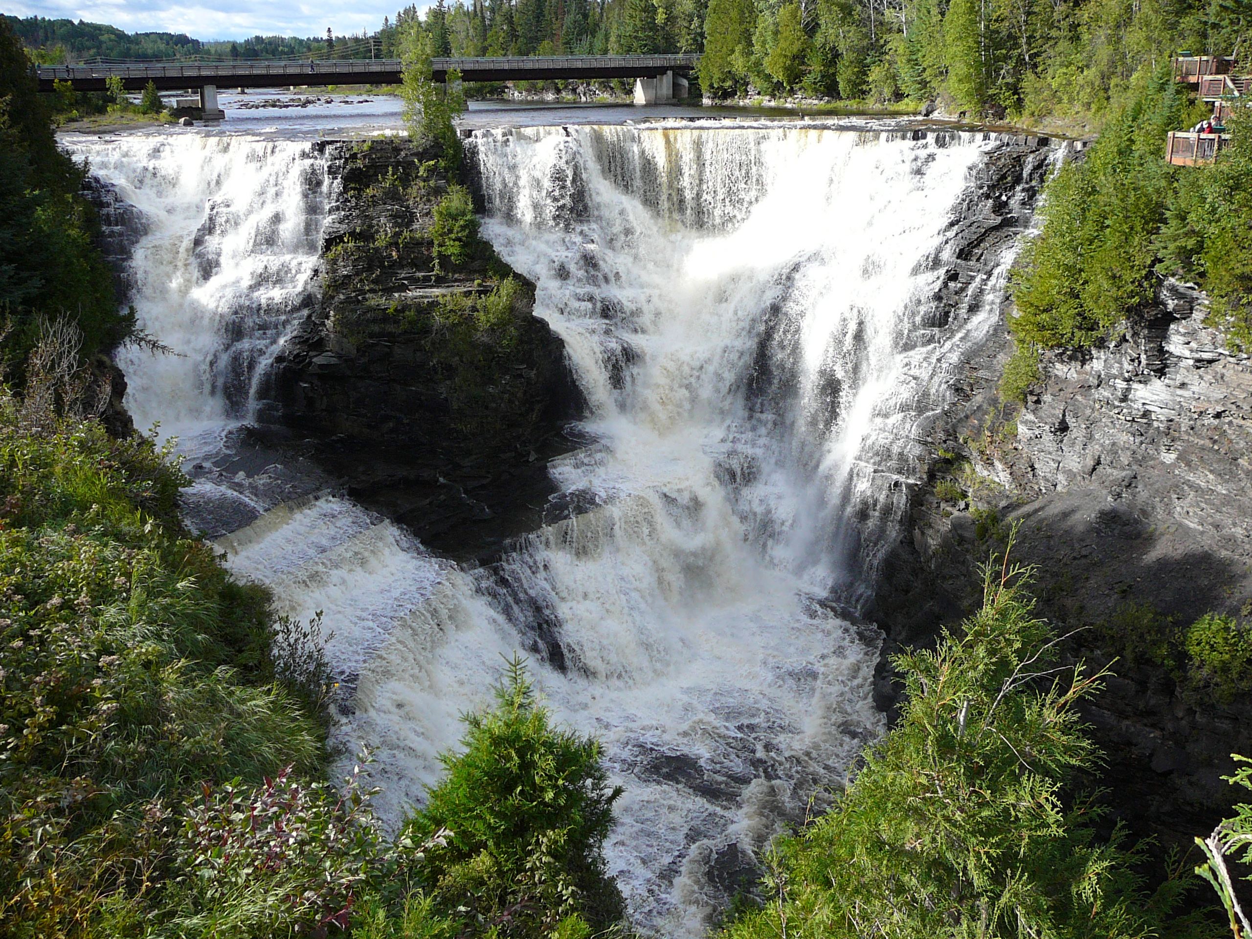 Kakabeka Falls; a tall, rocky double waterfall surrounded by cliffs and lush green forest