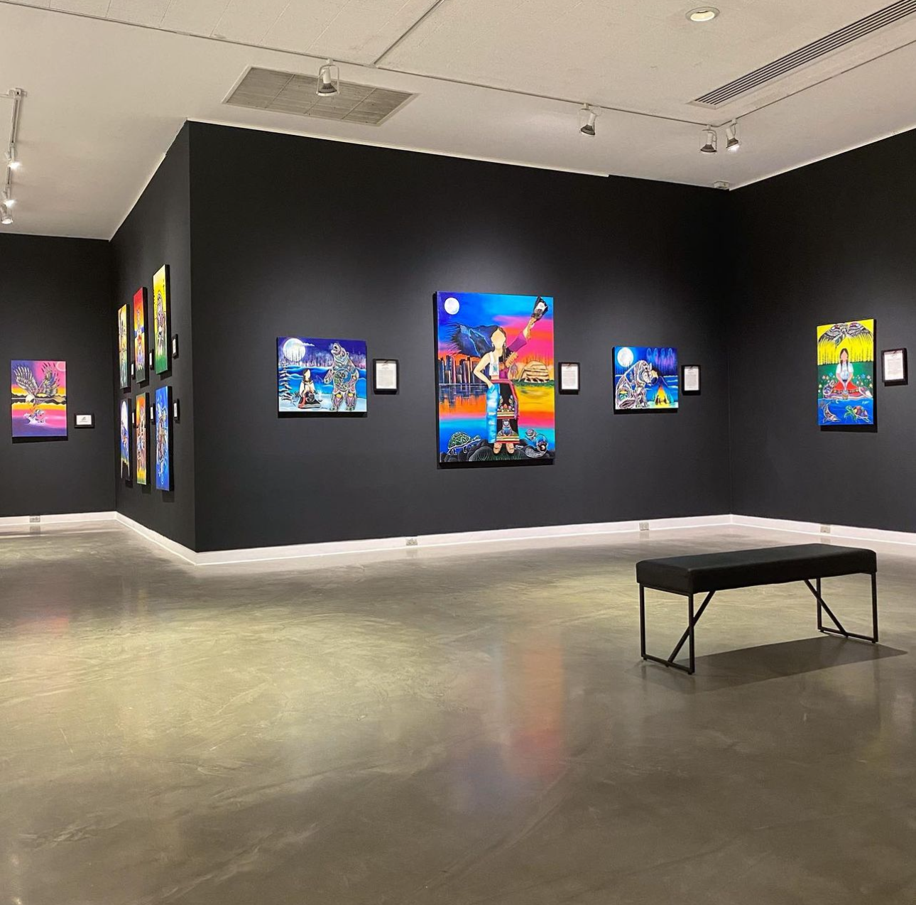  WKP Gallery; a large, open gallery space with black walls and potlights highlighting the brightly coloured indigenous art hung along the walls. 