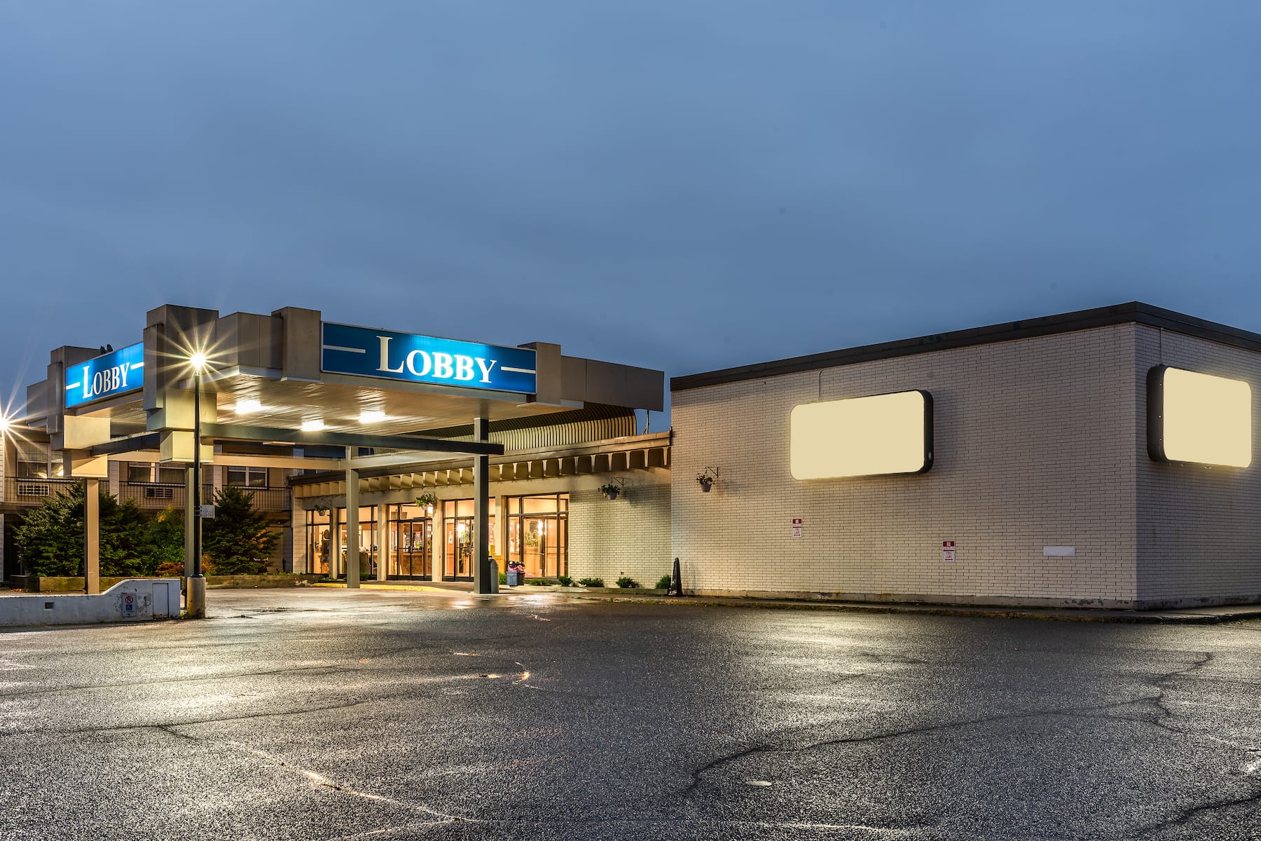 The exterior of the Ramada Wyndham Thunder Bay; a polished-looking and welcoming building with signs and lobby windows glowing in evening light. 