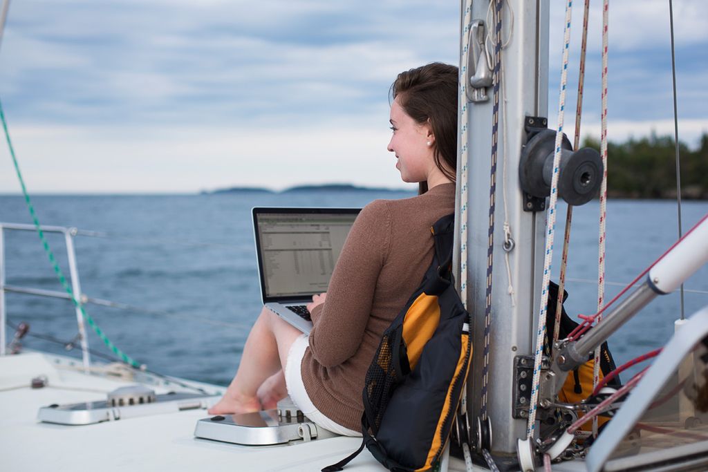 a woman smiling, working on a computer while sitting on a catamaran on Lake Superior.