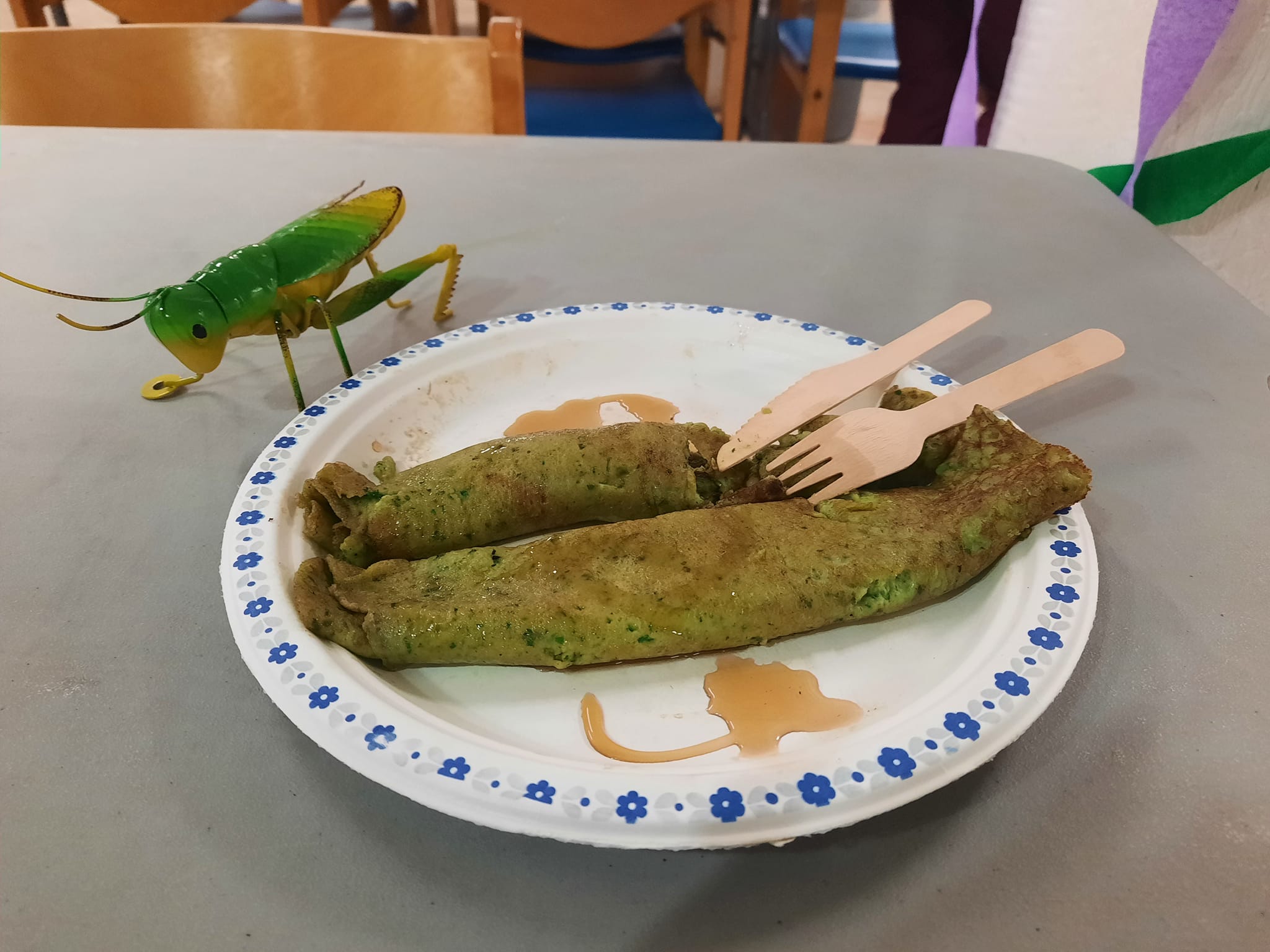 2 spinach Finnish pancakes on a plate, next to a large toy grasshopper