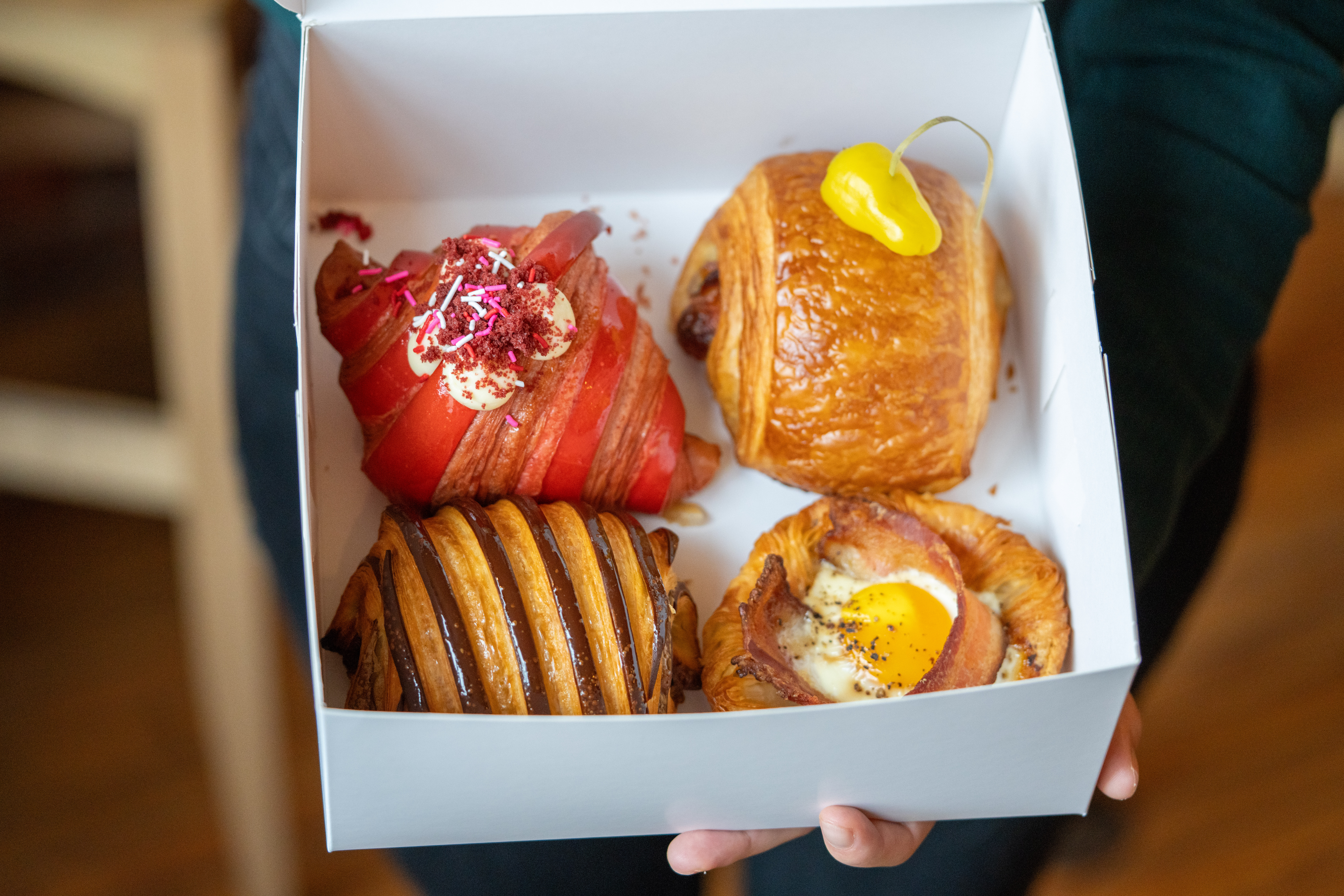 hands holding open a box of elegantly decorated pastries