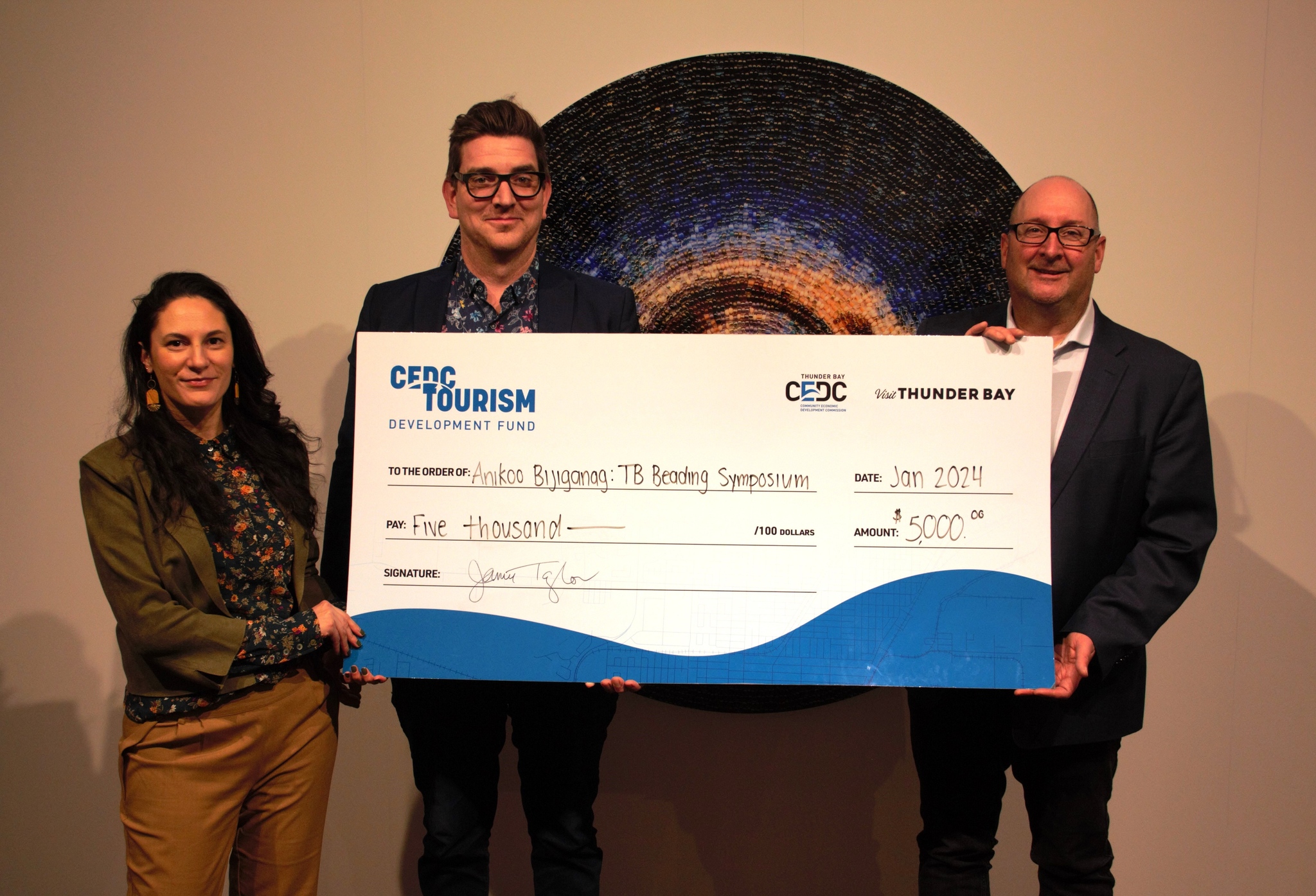 CEDC representatives awarding a giant cheque to a grant recipient; two smiling men and a smiling woman are holding a novelty cheque representing their grant. 