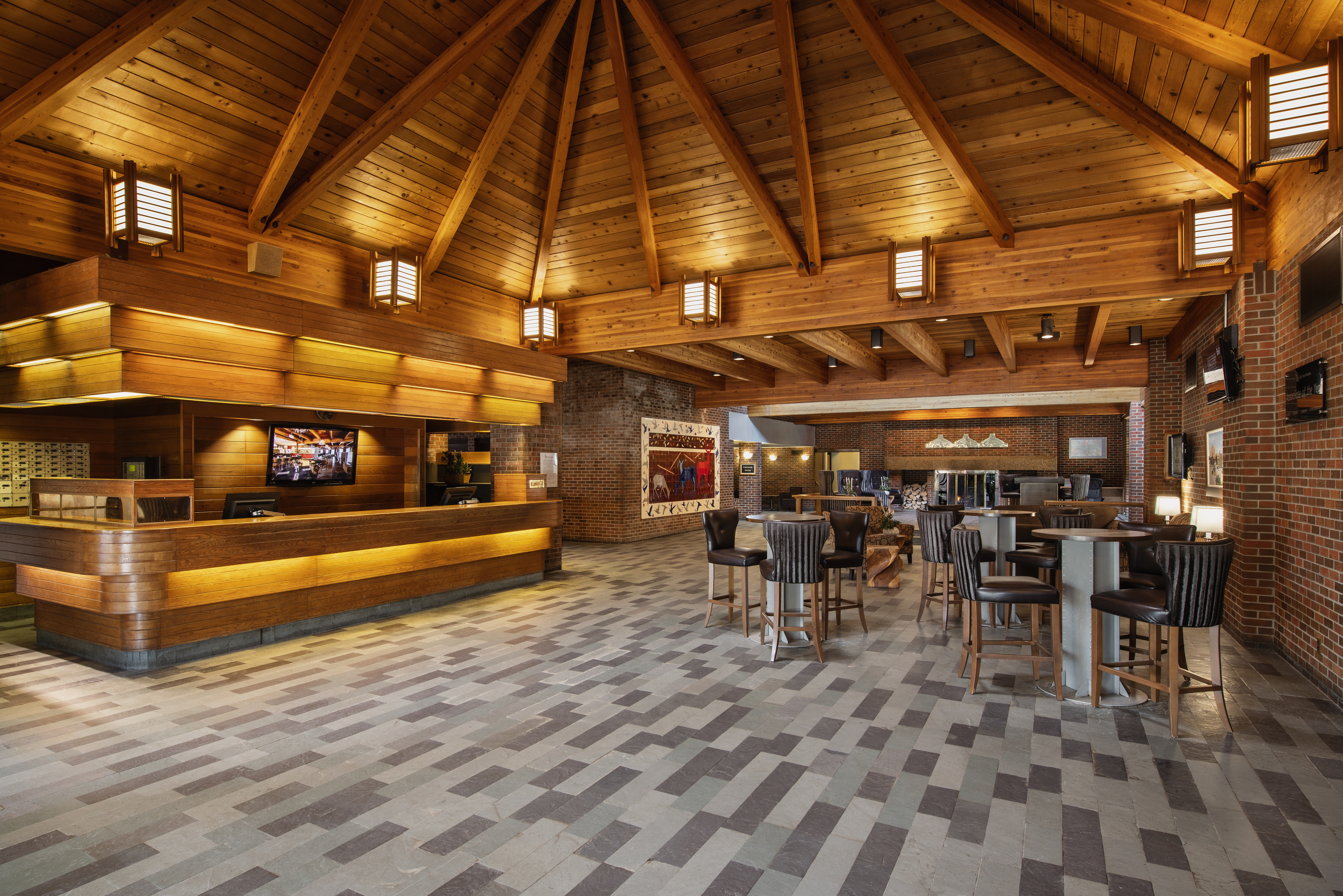 The lobby of the Valhalla Inn Thunder Bay; an large, impressive looking room with a high-peaked wooden beam ceiling circled by soft lamp light, a lit wooden front desk and polished tiled floors.