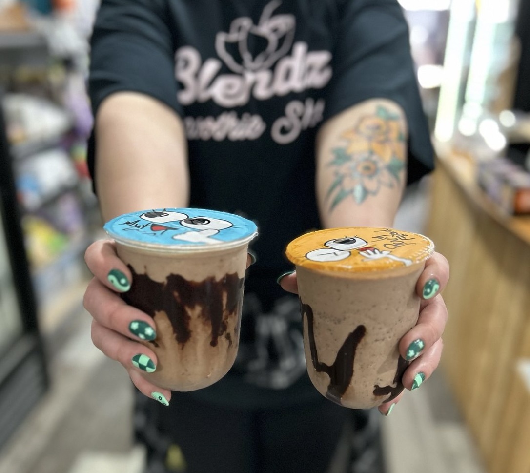 a pair of hands on a person wearing a Blendz t-shirt, holding two dairy-free milkshakes—one mint chocolate chip and the other rocky road.