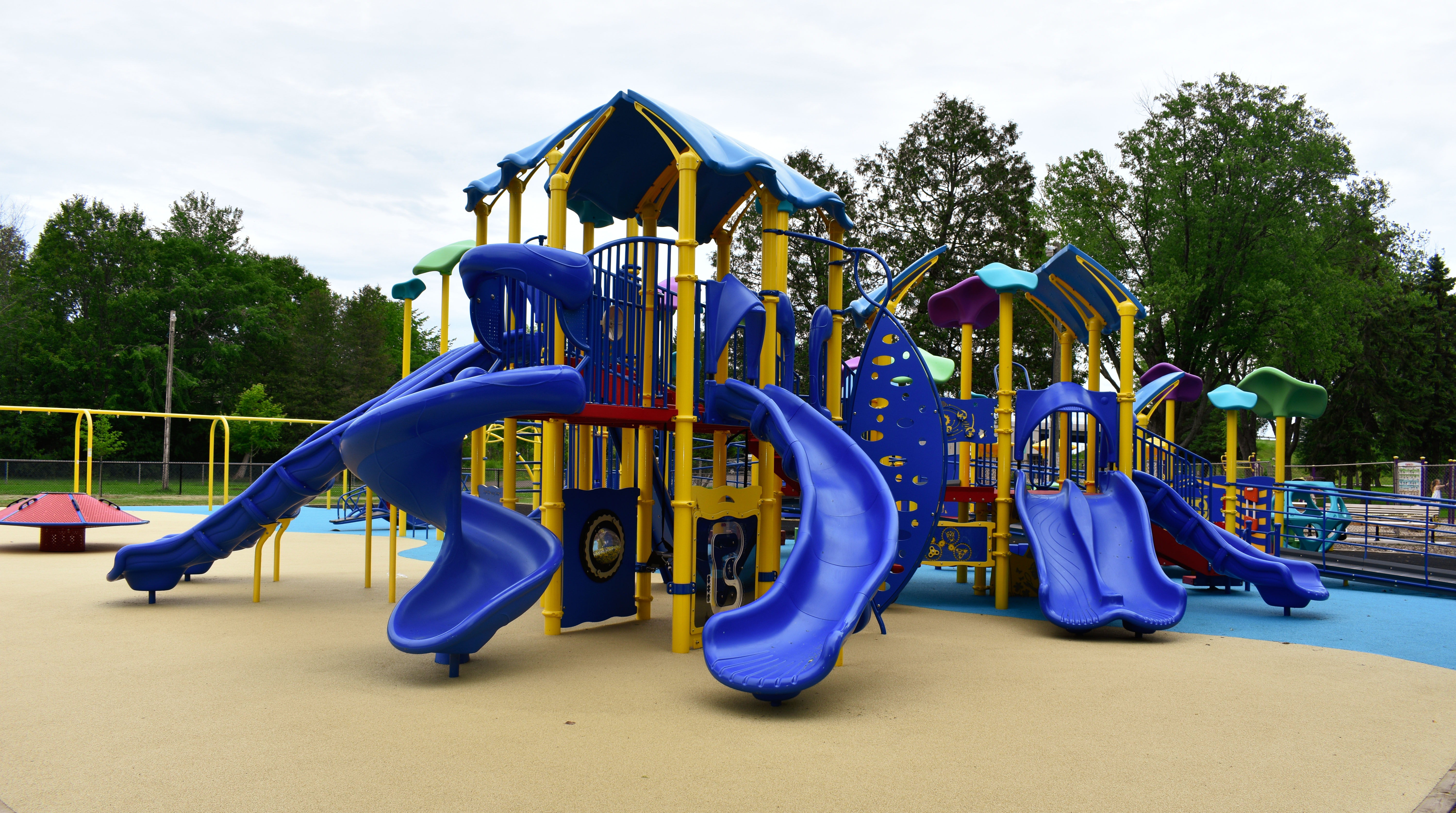 Lee Park; a clean, new playground with multiple slides and climbing apparati surrounded by green trees.