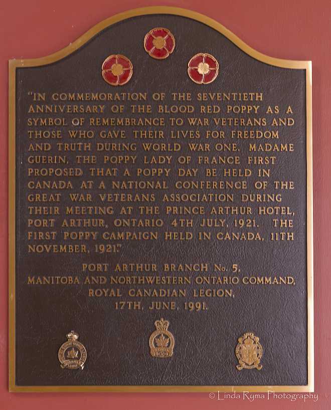 The plaque commemorating the adoption of the poppy as a symbol of remembrance in Thunder Bay; a red, gold and black informational plaque decorated with 3 red and gold poppies. 