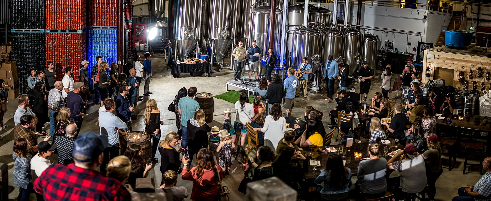 Taproom at Sleeping Giant Brewery; a large, brightly-lit and modern looking room with beer brewing equipment on one side, and rows of chairs and people filling the room.