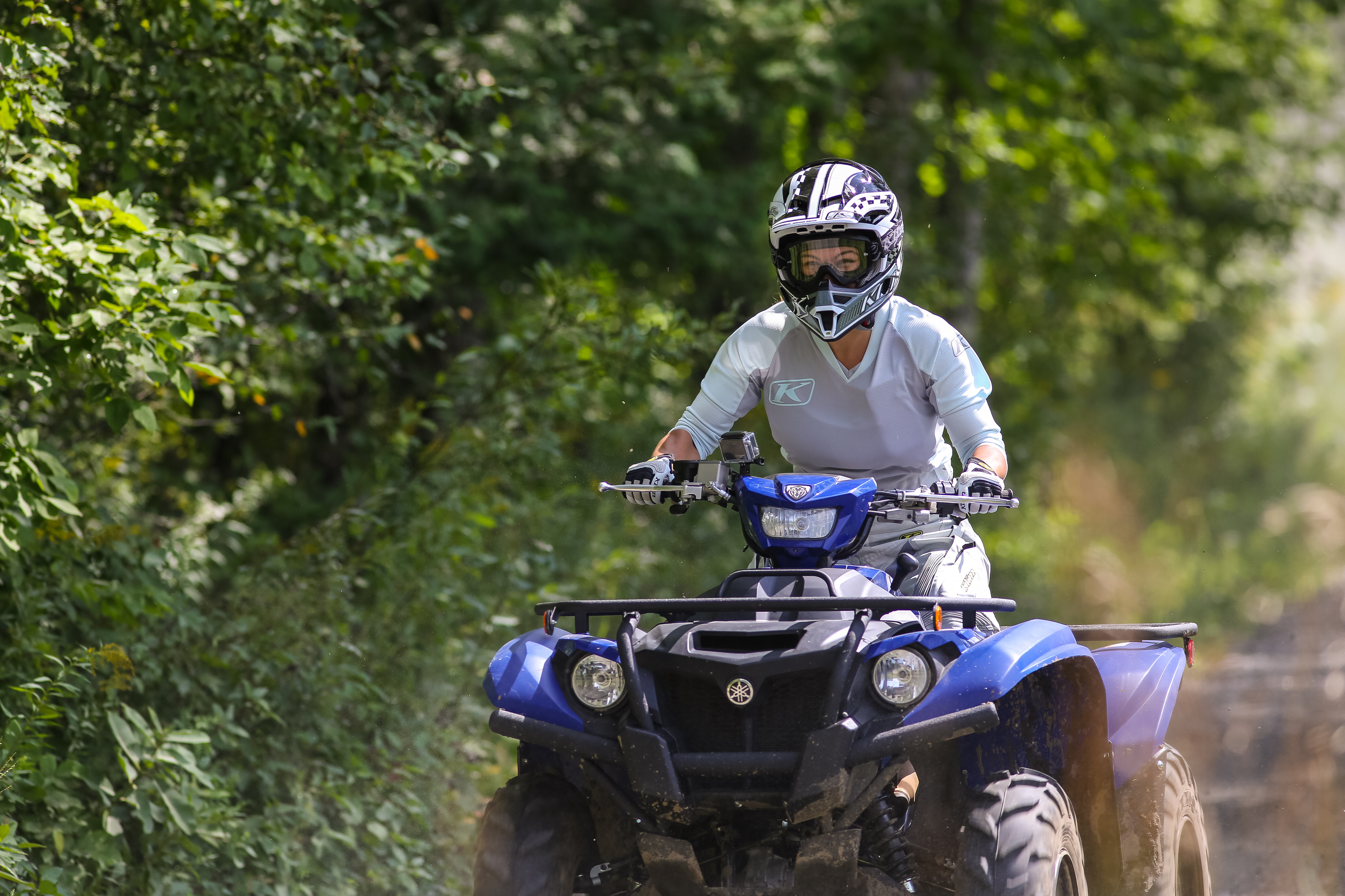 A rider standing up while driving an ATV on a trail surrounded by lush green forest.