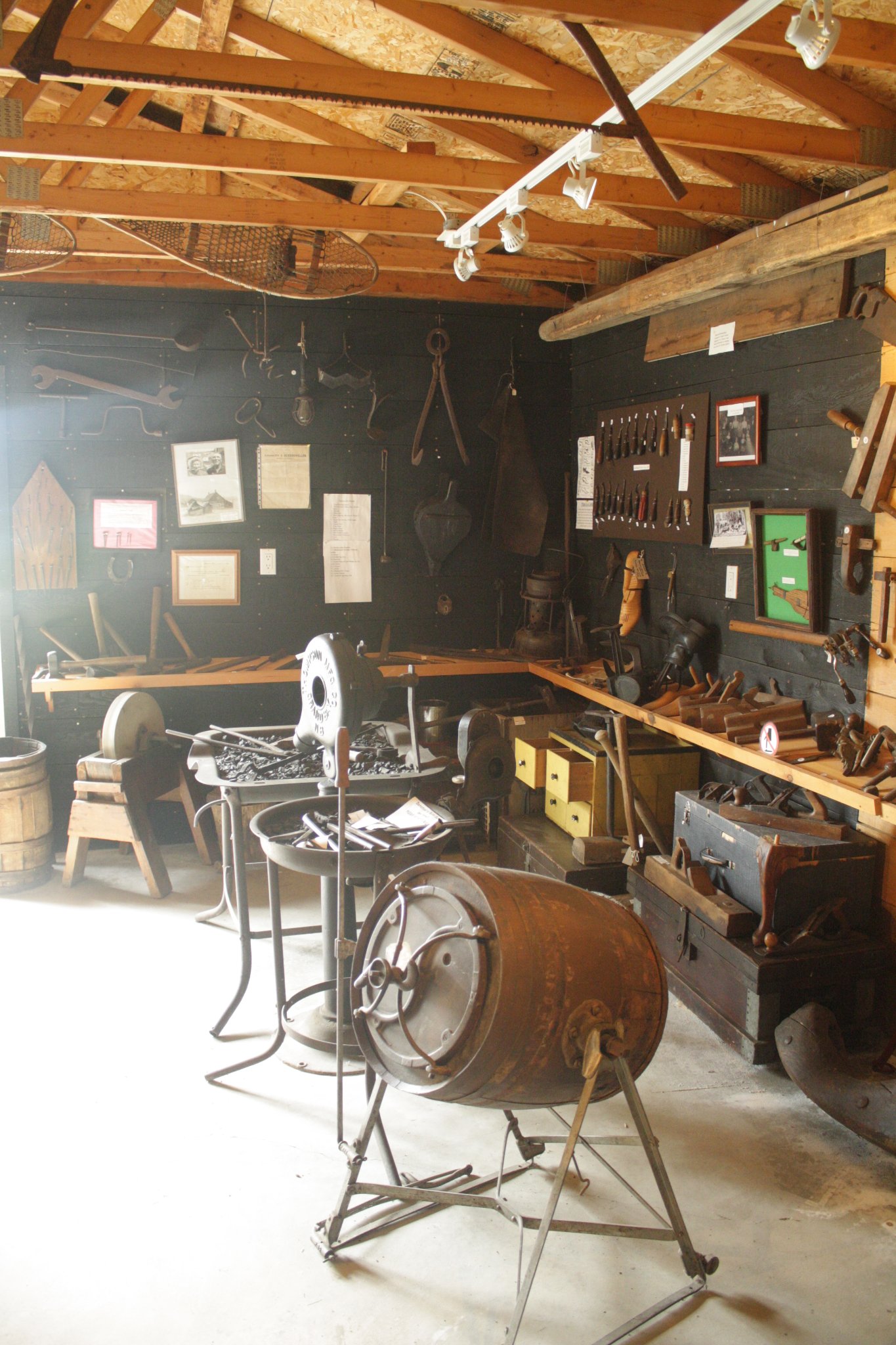 The Blacksmith & Cobbler's Exhibit at the Nipissing Township Museum; the interior of a wooden shed lit by sunlight, filled with antique blacksmithing and cobbler's tools. 