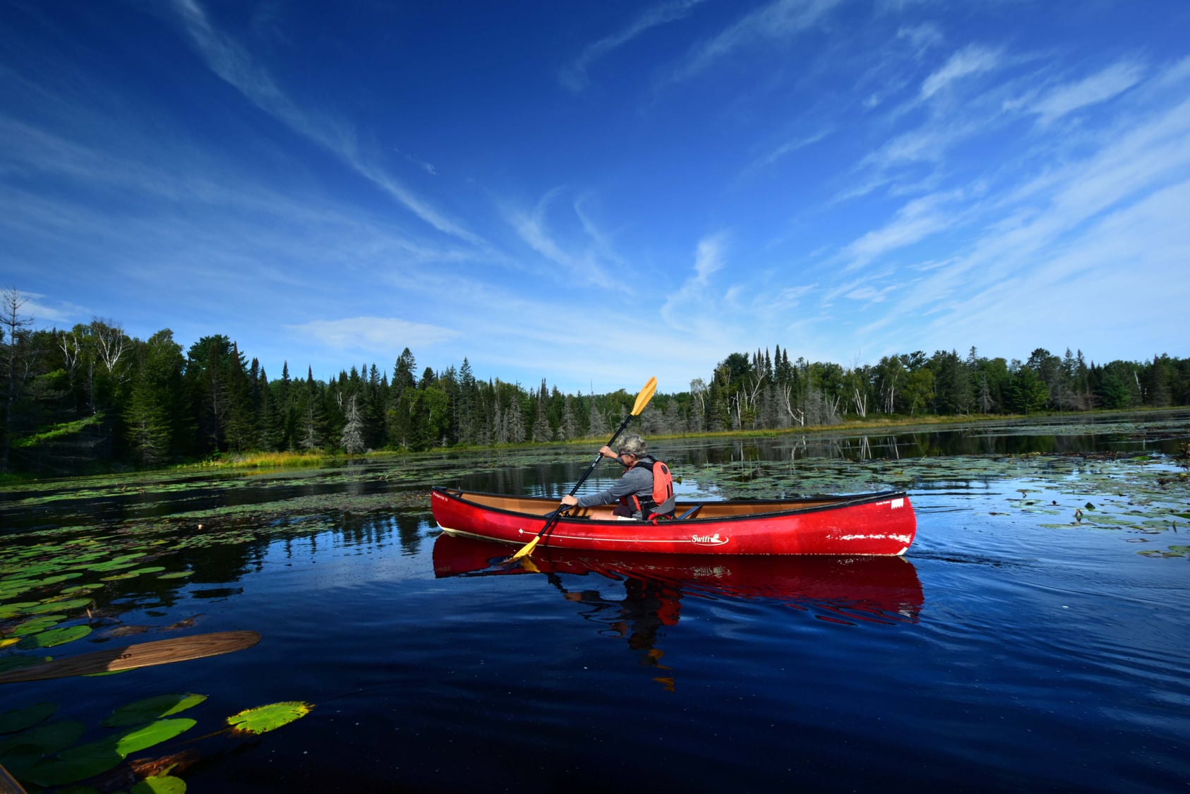 Man in a red canoe with a blue sky behind him.