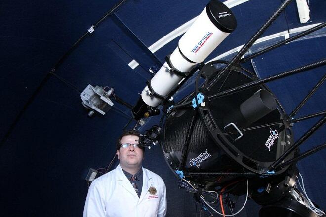 A man wearing glasses and lab coat peers through a huge observatory telescope.