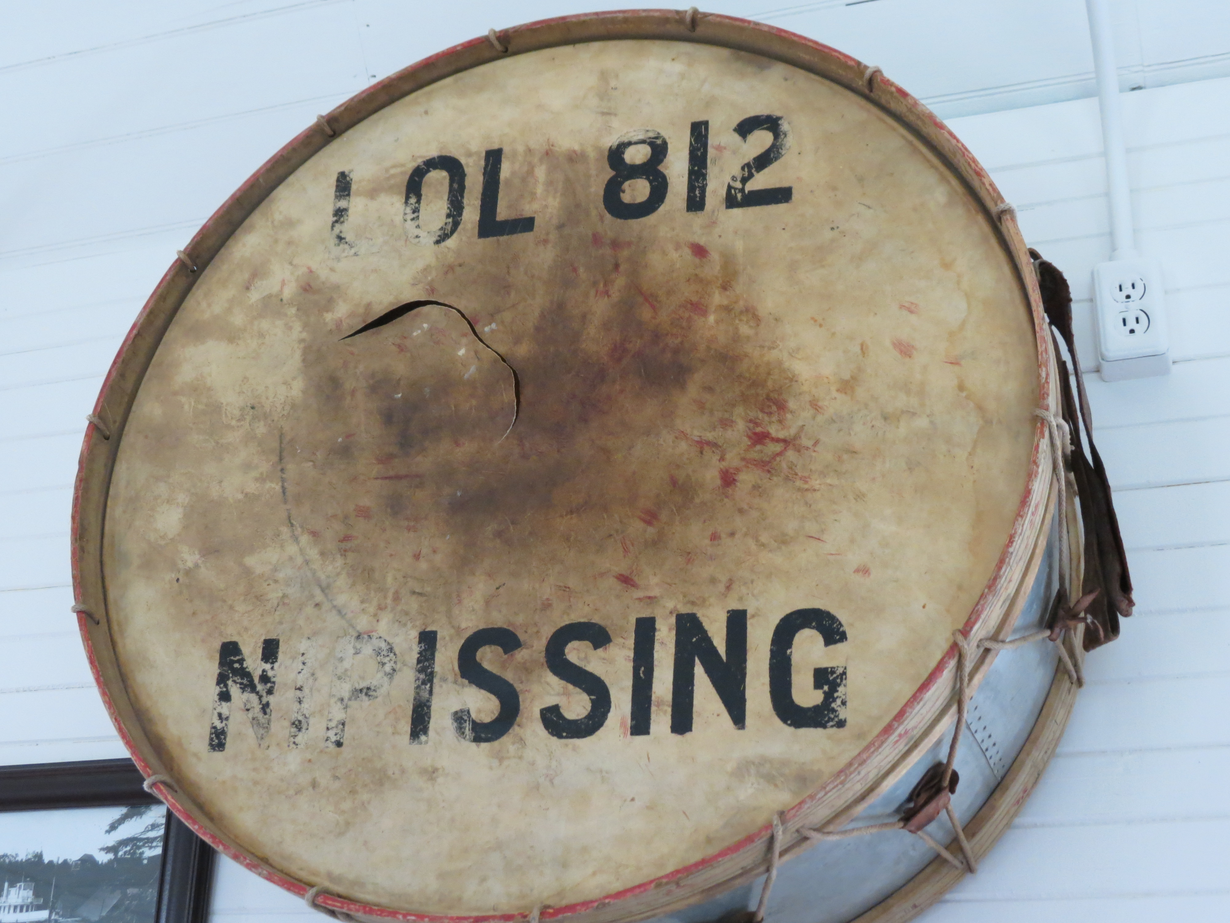an antique drum on display at the Nipissing Township Museum, with the words "LOL 812 Nipissing" printed on the aged top skin.