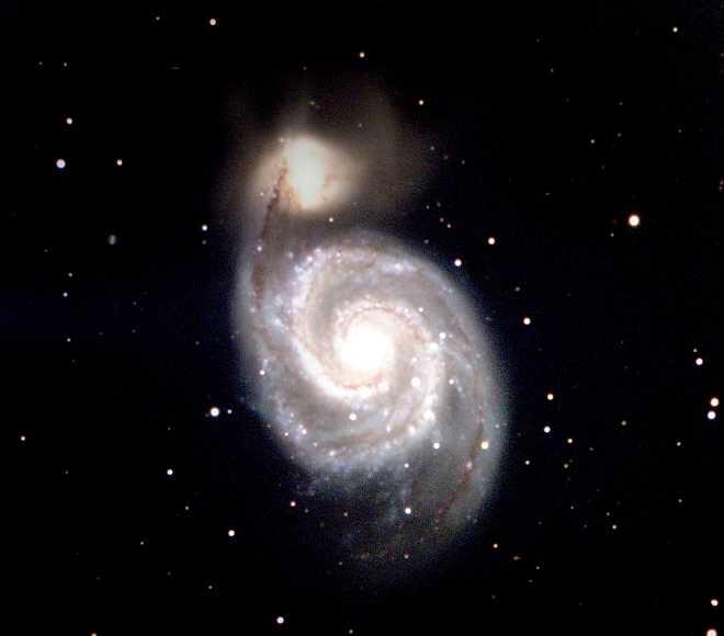 a galaxy of white light in space, swirling from its center point in a spiral pattern, surrounded by dots of white stars. 