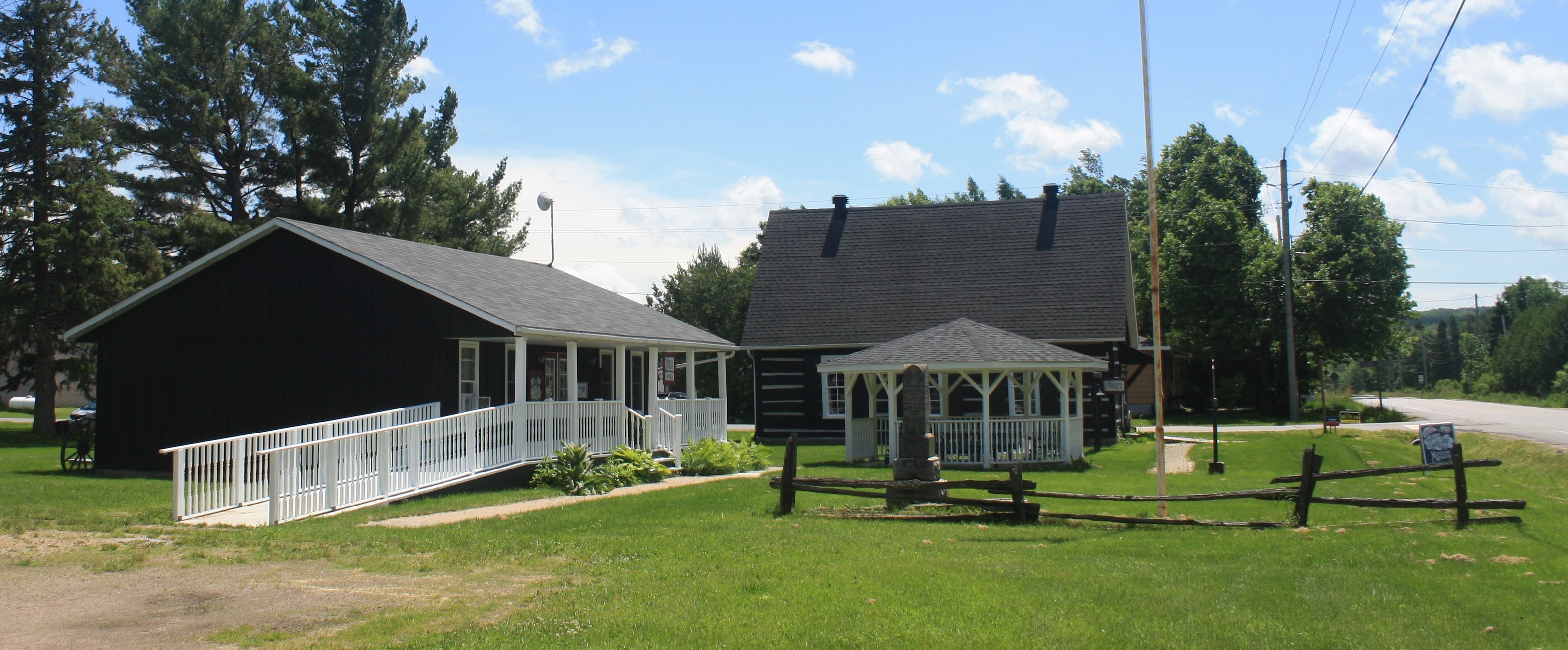 Three structures at the Nipissing Township Museum; the Gift Shop, the gazebo and the church building on a sunny summer day.