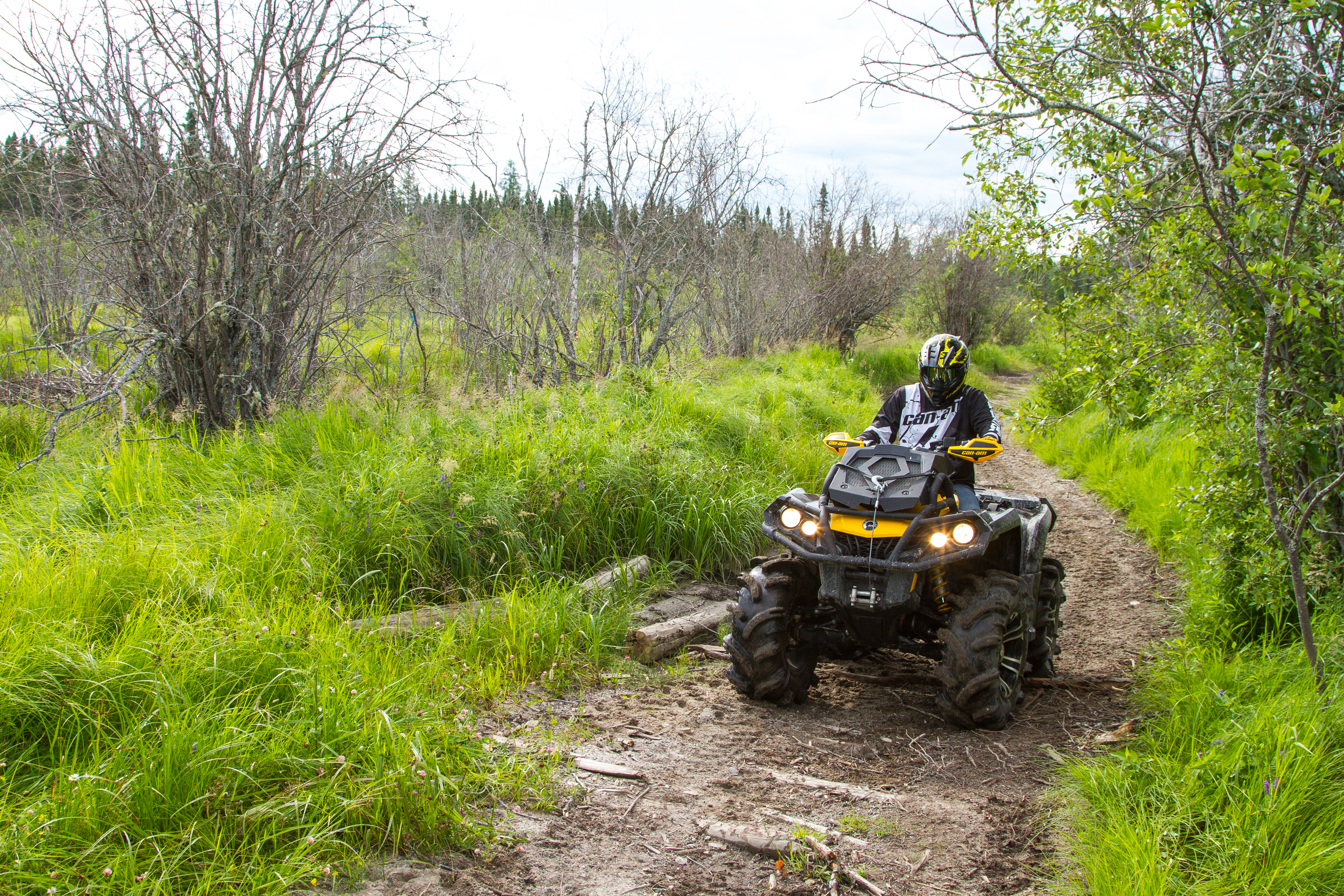 A person on an ATV riding down a muddy trail surrounded by lush greenery.