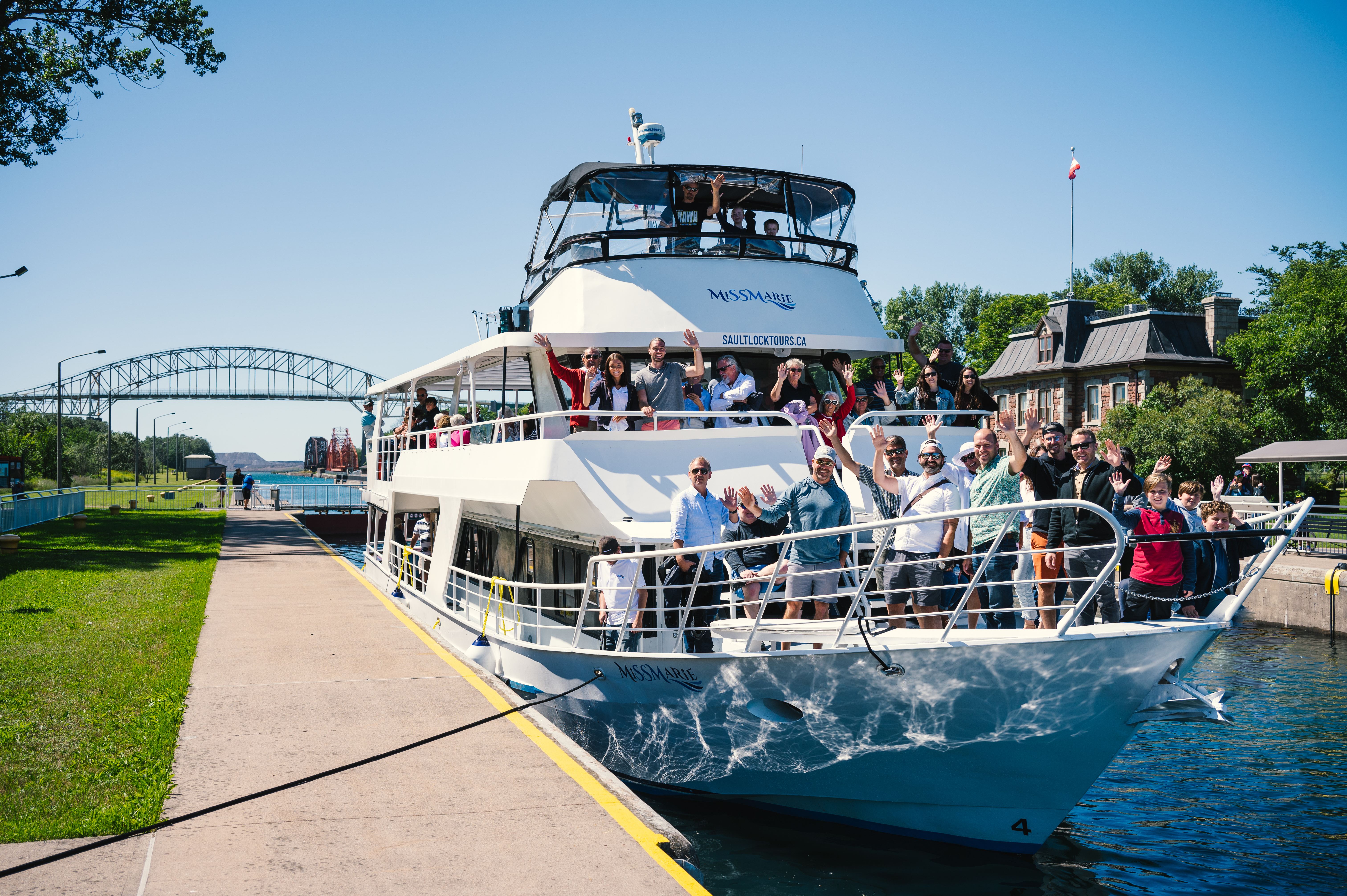 A group of people on a white tour boat docked in a canal with a bridge in the background.