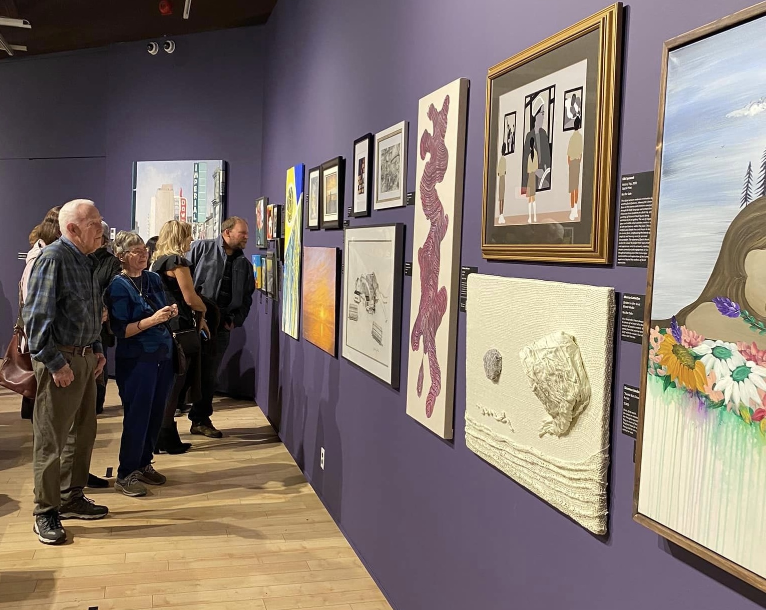 patrons enjoying and discussing the many paintings hung in front of them on the gallery walls in the Art Gallery of Algoma.