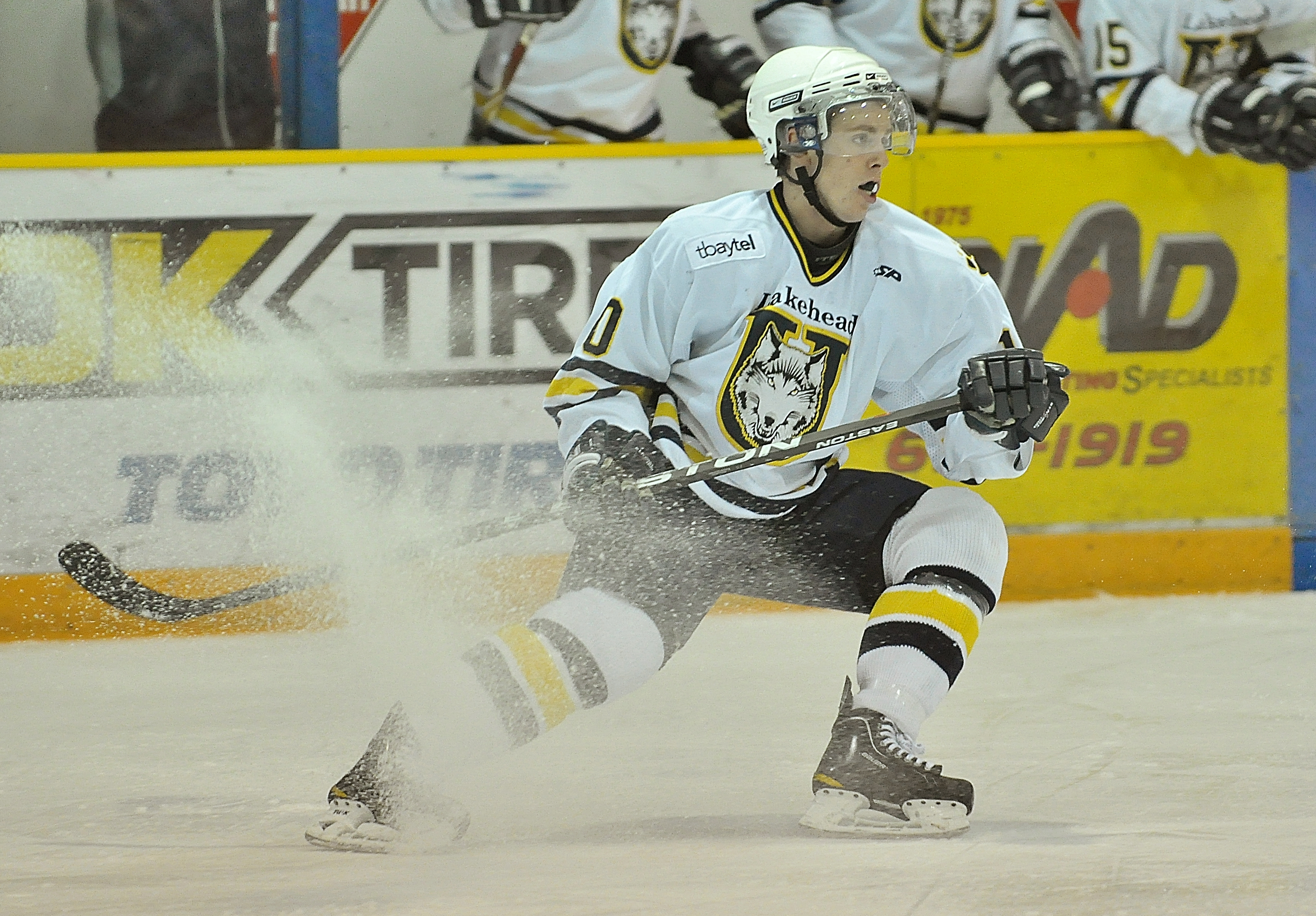 A Thunderwolves player makes a hard stop on the ice, snow spraying up in a cloud.