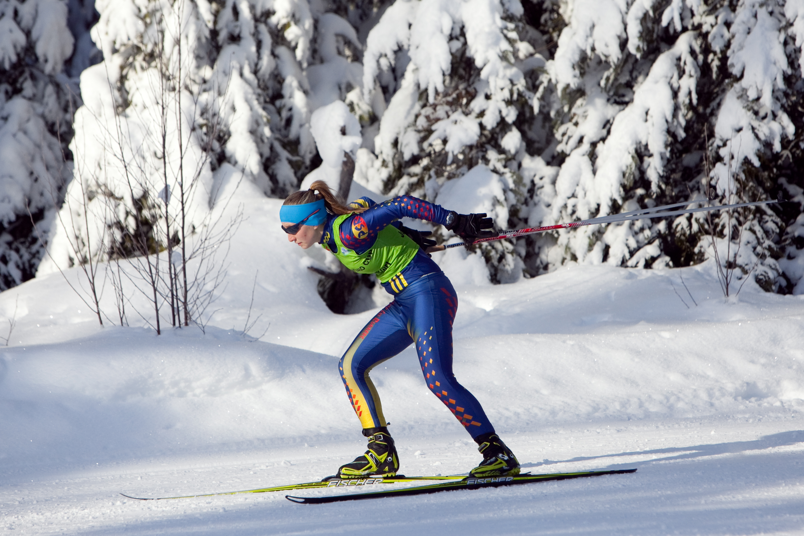 a skiier is dressed in a blue and green ski suit and is skiing a along a trail