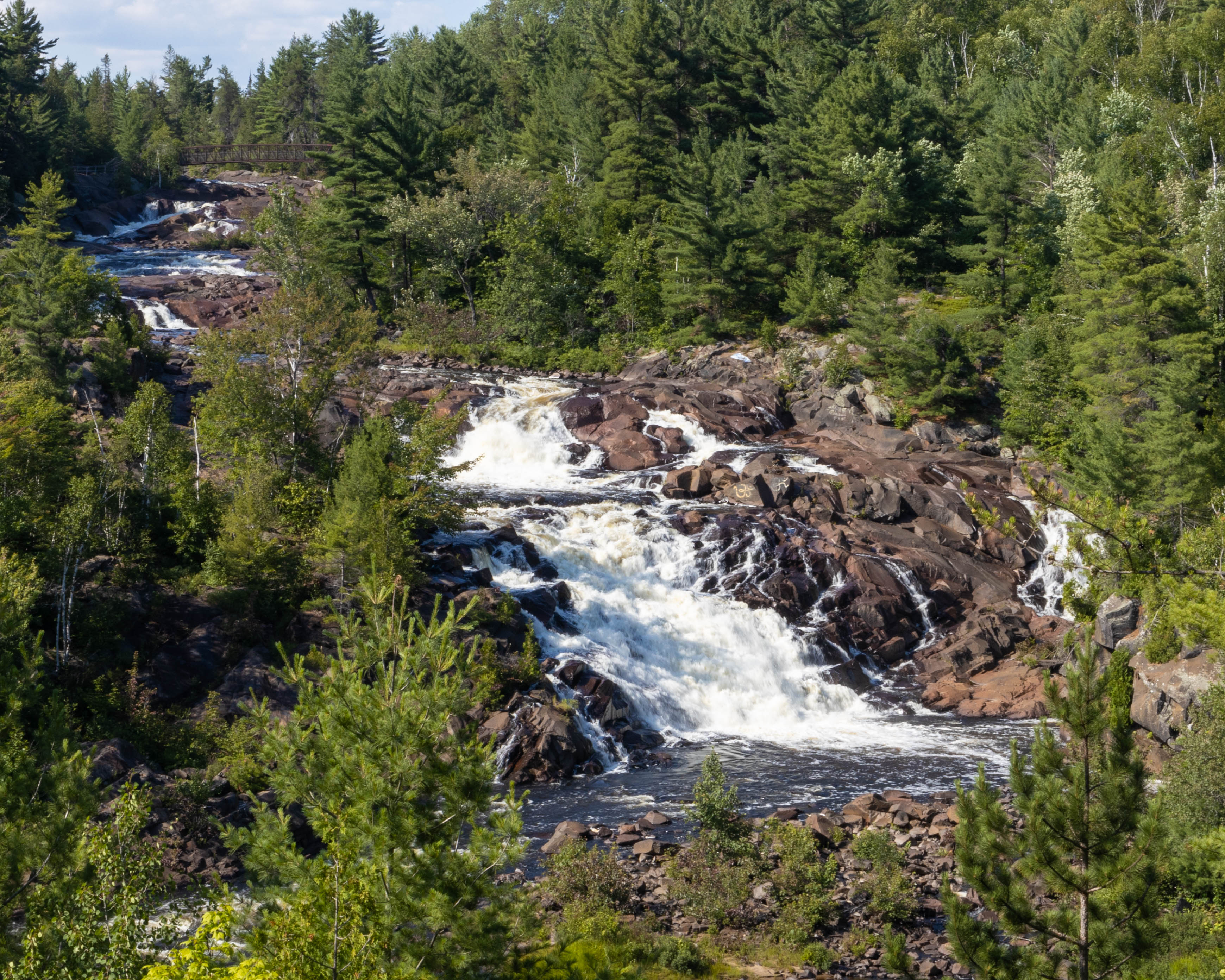 High Falls; a long tumbling waterfall down a rocky riverbed surrounded by thick pine forest.