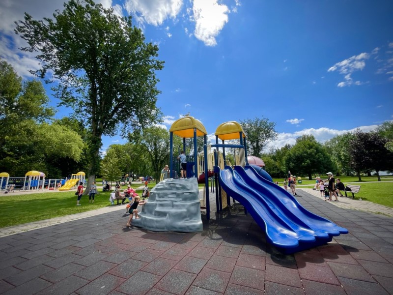 A pair of blue plastic slides on a playground with children visible in the background. 