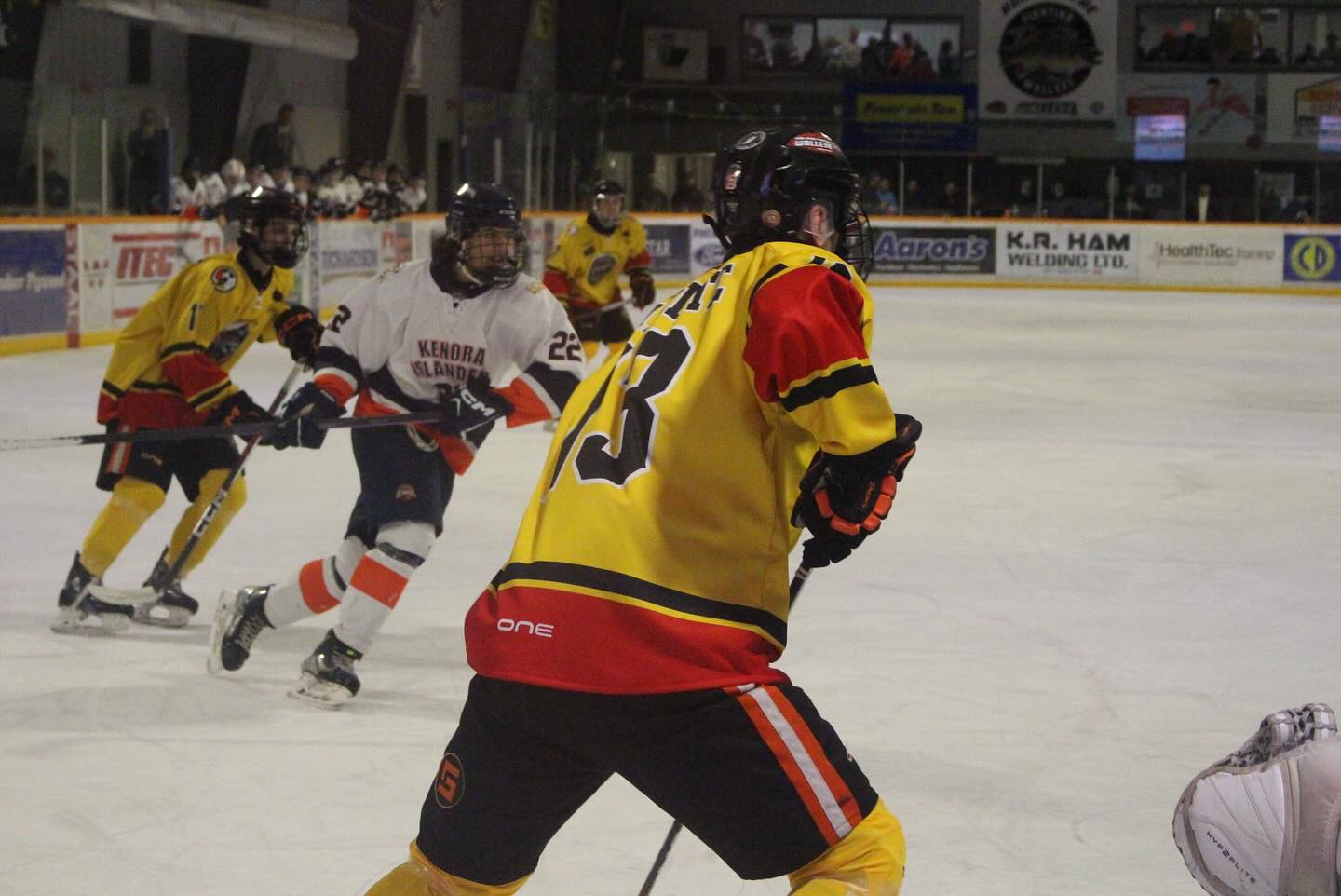 The Kam River Fighting Walleye hockey team skating rapidly to head off a member of the Kenora team, determined and focused looks on their faces.