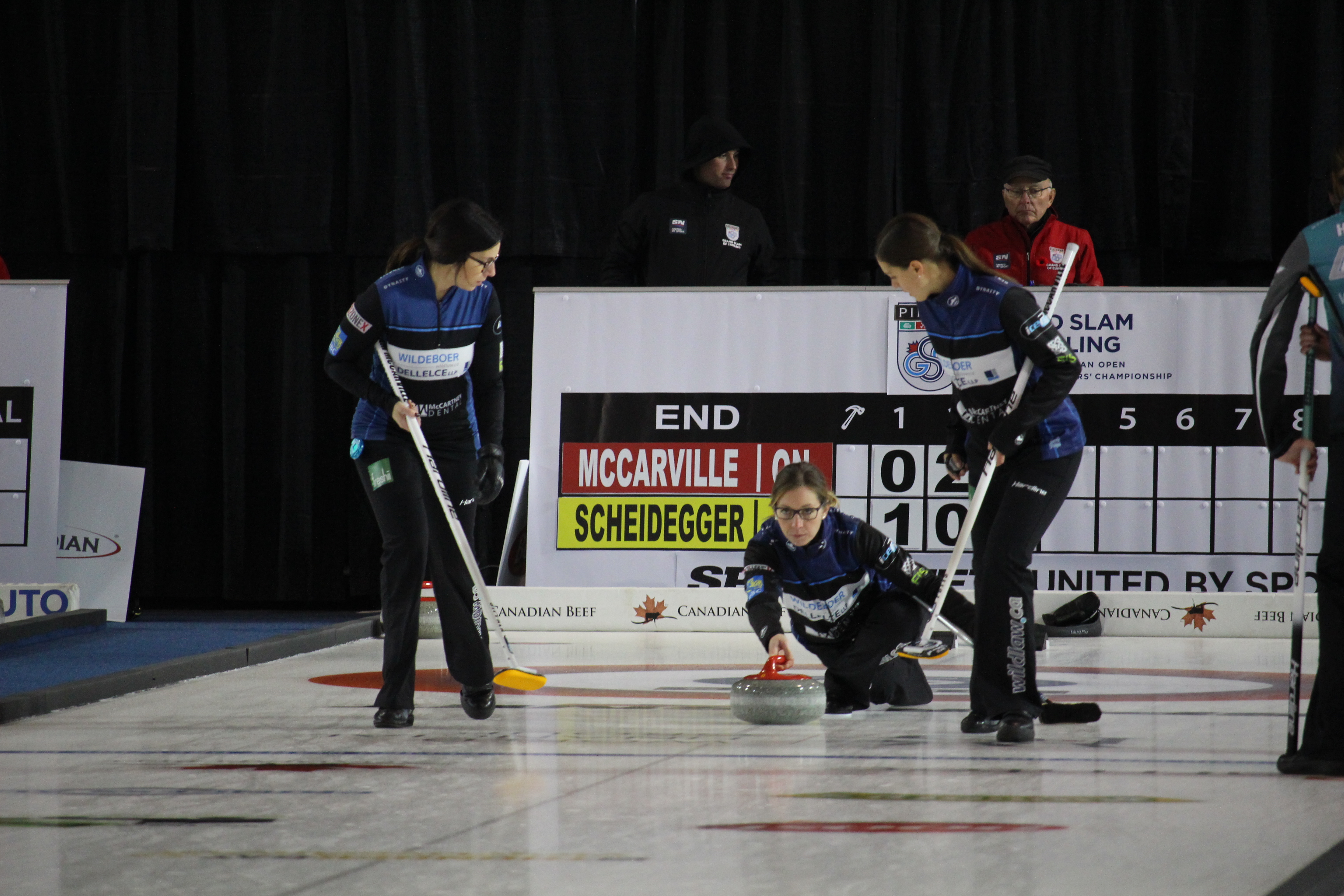 Krista McCarville throwing a curling rock with determination and focus as her team mates watch over her.