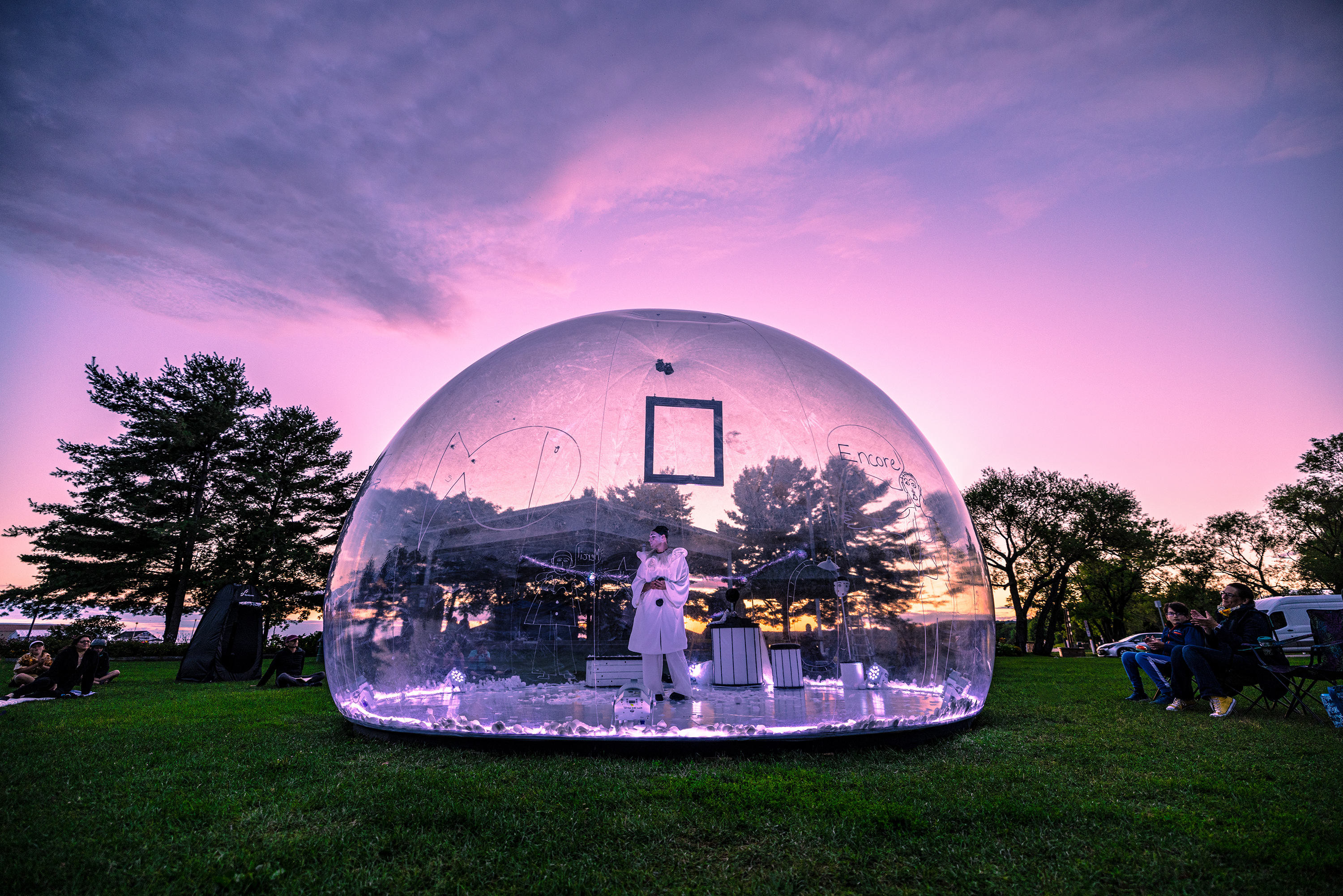 An artist performing in a clear geodome against a purple sunset.