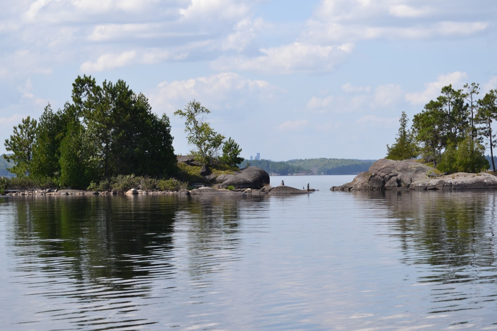 2 small, rocky islands covered in green trees in the calm water of Lake Wanapitei.